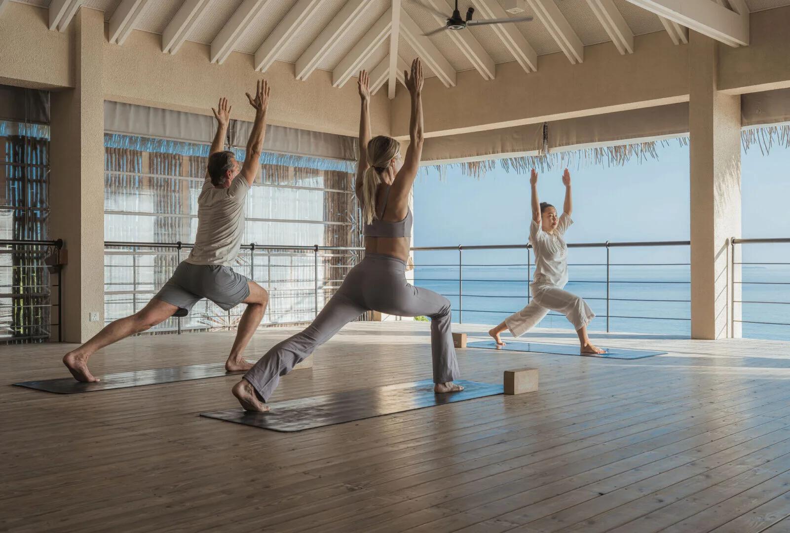 Guests in a yoga class inside an open-air overwater pavilion overlooking the ocean