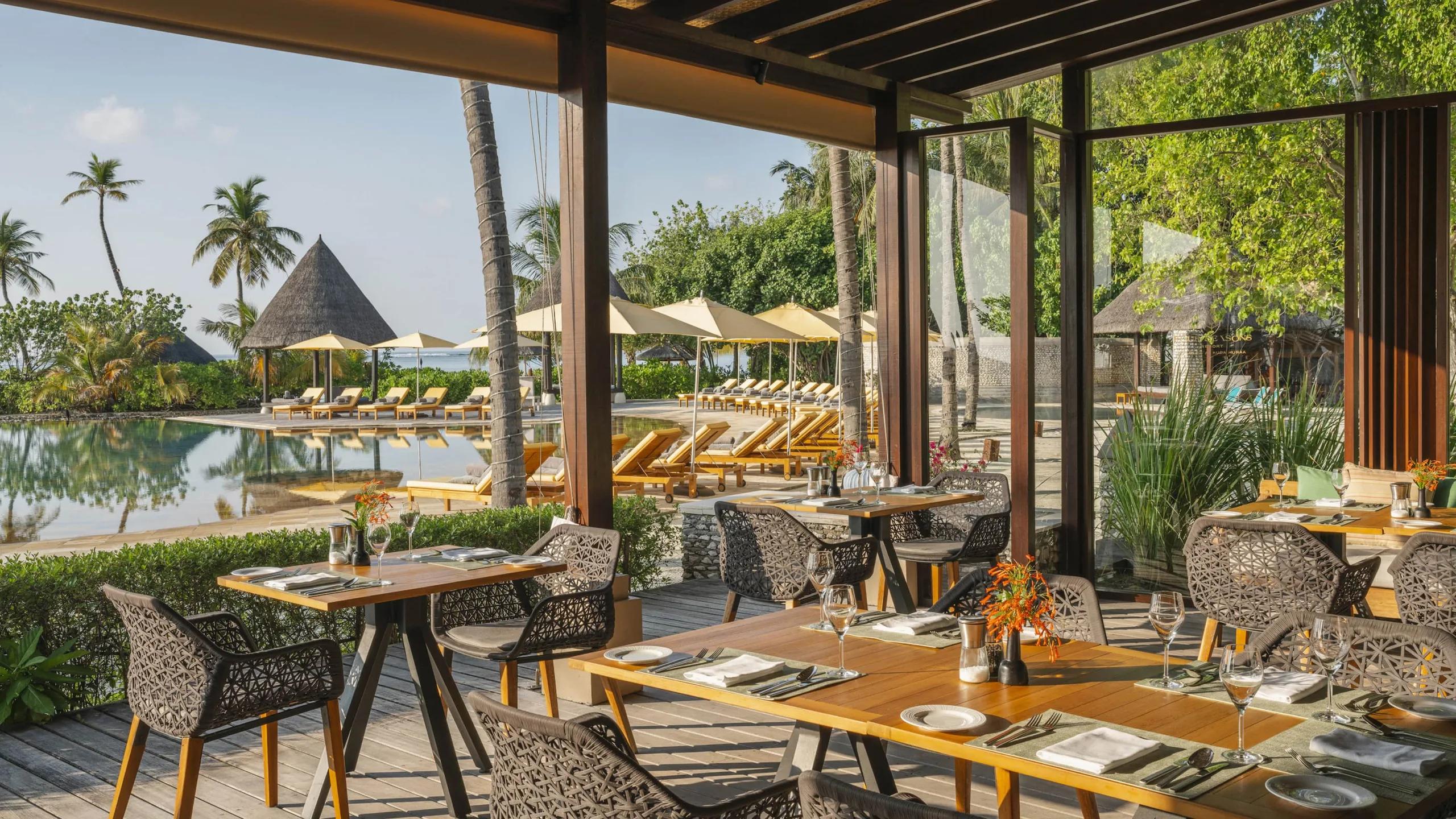Café Huraa's terrace seating beside the infinity pool, thatched cabanas beyond