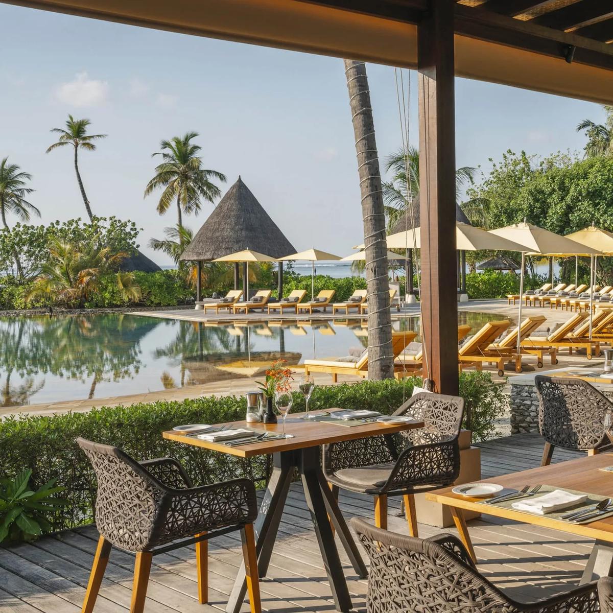 Café Huraa's terrace seating beside the infinity pool, thatched cabanas beyond