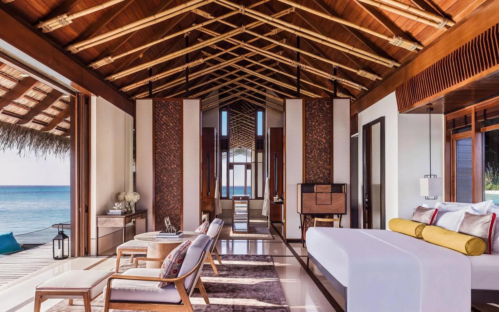 The bedroom of a Water Villa at One&Only Reethi Rah, opening onto its net hammock deck over the lagoon at sunset