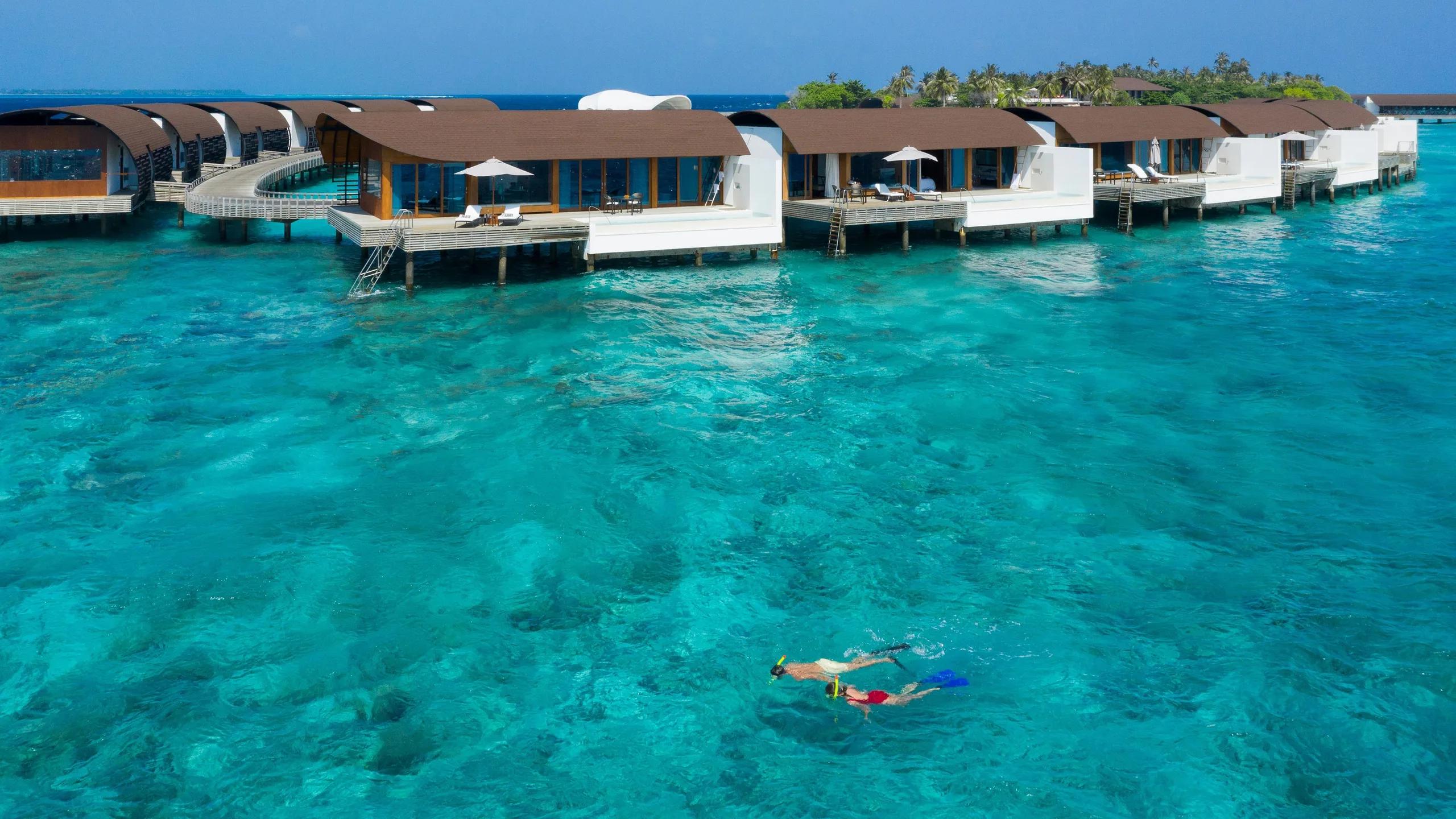 Two snorkellers crossing the lagoon beneath the overwater villas' jetty