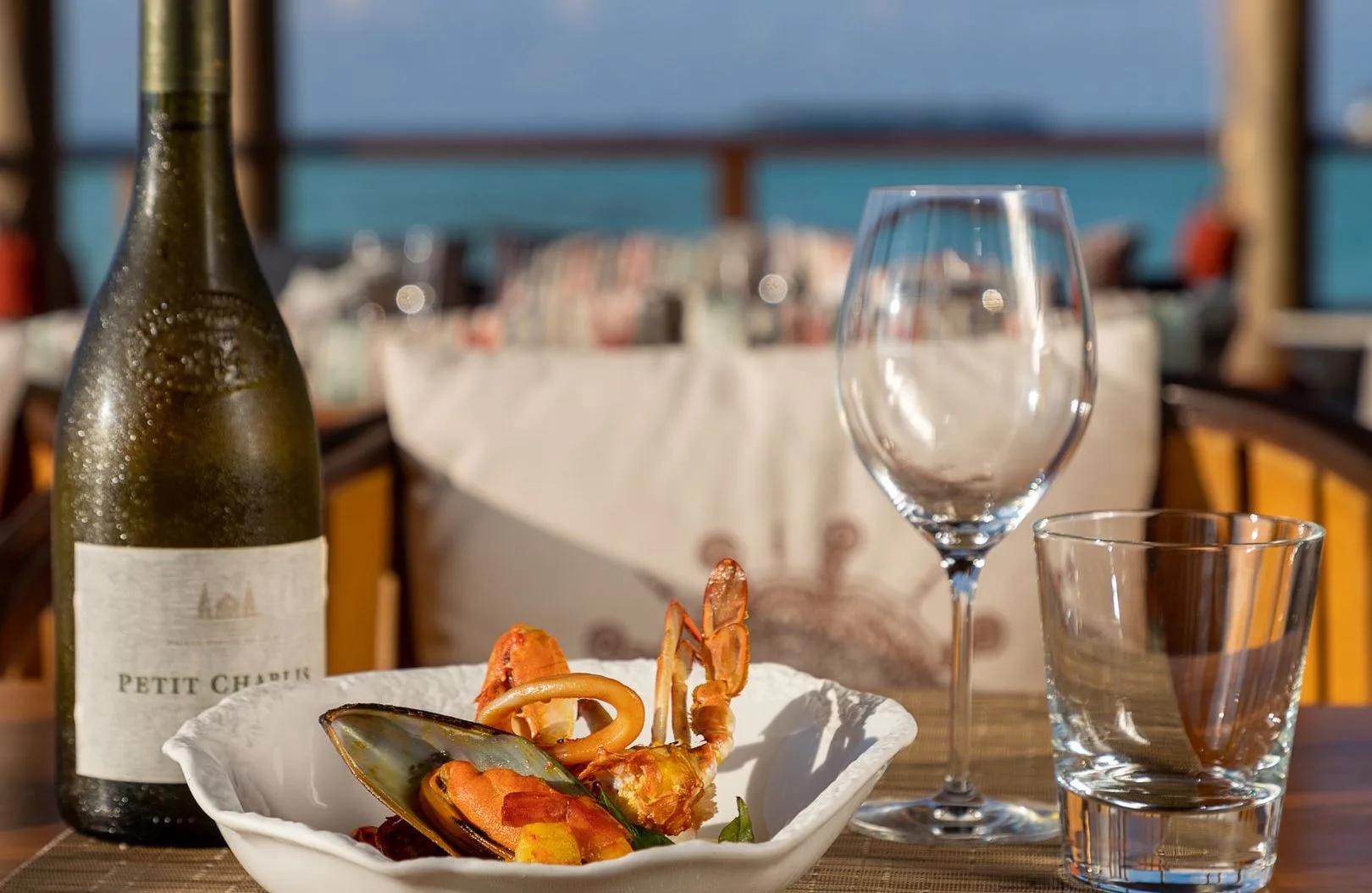 A plate of mud crab, mussels and calamari with a glass of white wine, on an overwater deck with a crab-motif cushion