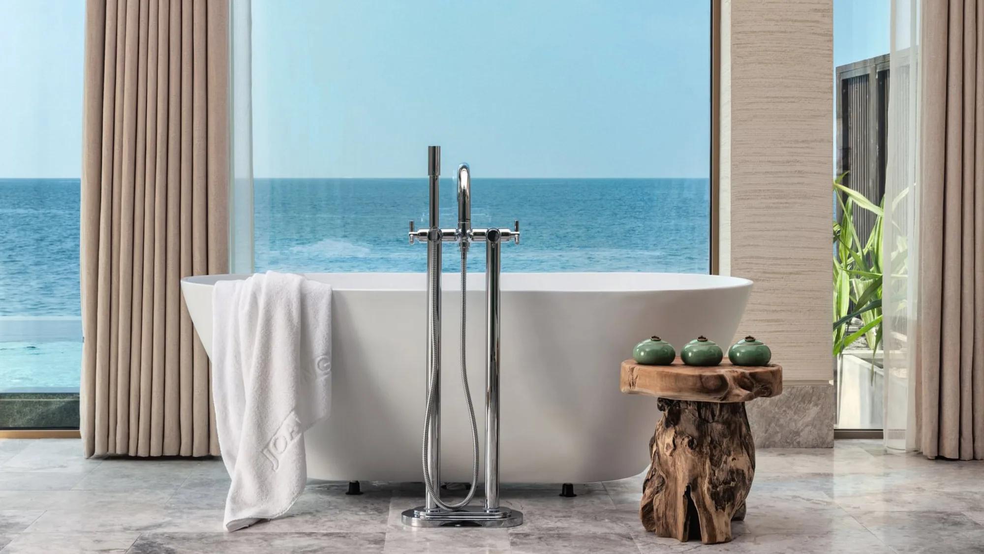 A freestanding bathtub facing full-height windows onto the open ocean in a Grand Ocean Pool Villa at Joali Being
