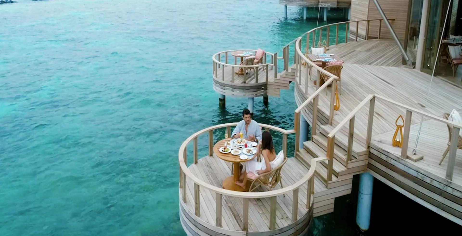 A couple dining at a private curved table on Zeytoun's overwater deck, the lagoon on all sides.