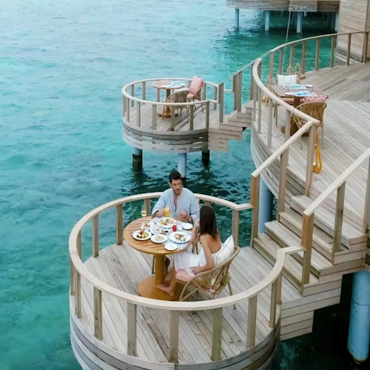 A couple dining at a private curved table on Zeytoun's overwater deck, the lagoon on all sides.