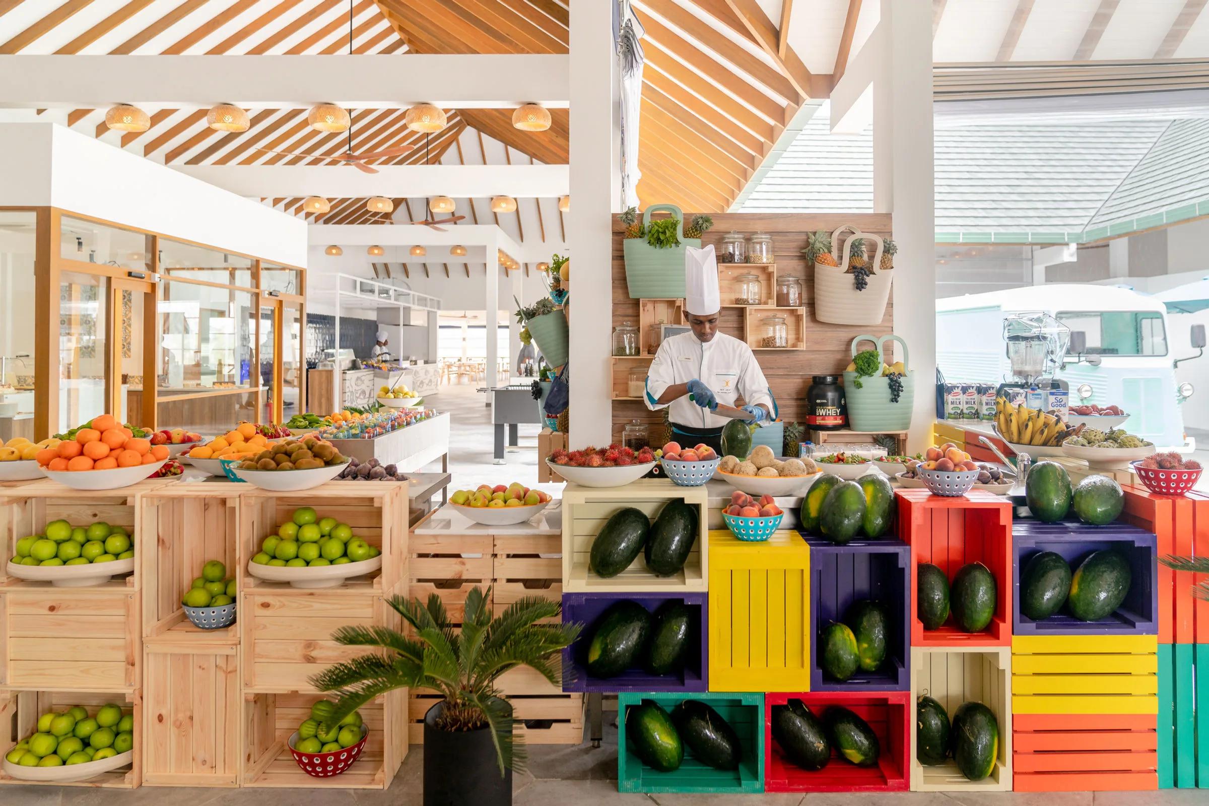 The Market's colourful fruit and produce stations, crates of avocados, mangoes and citrus stacked beside a chef at work