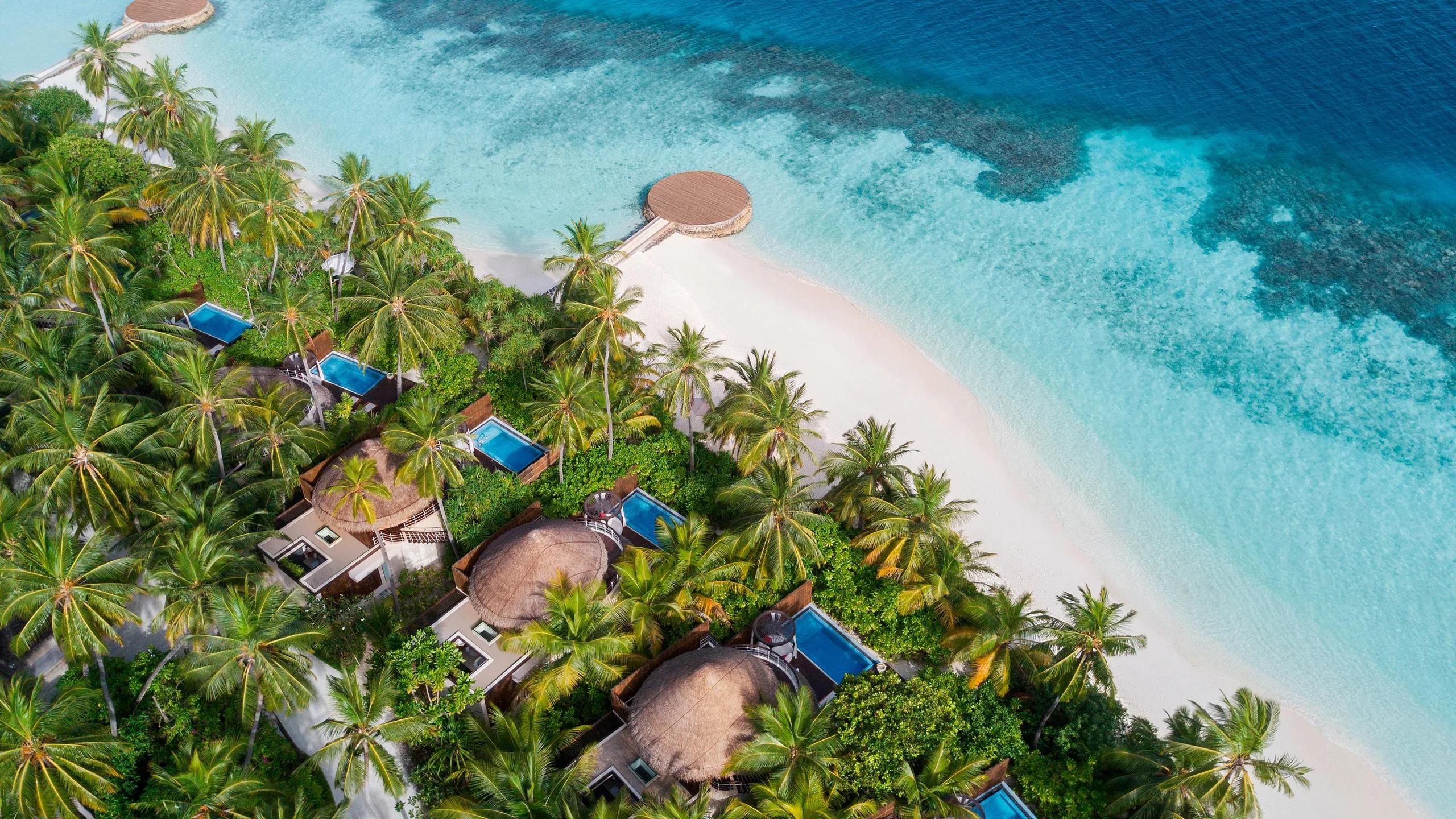 Aerial view of W Maldives' overwater villas and beach, the reef shading from pale turquoise to deep blue beyond