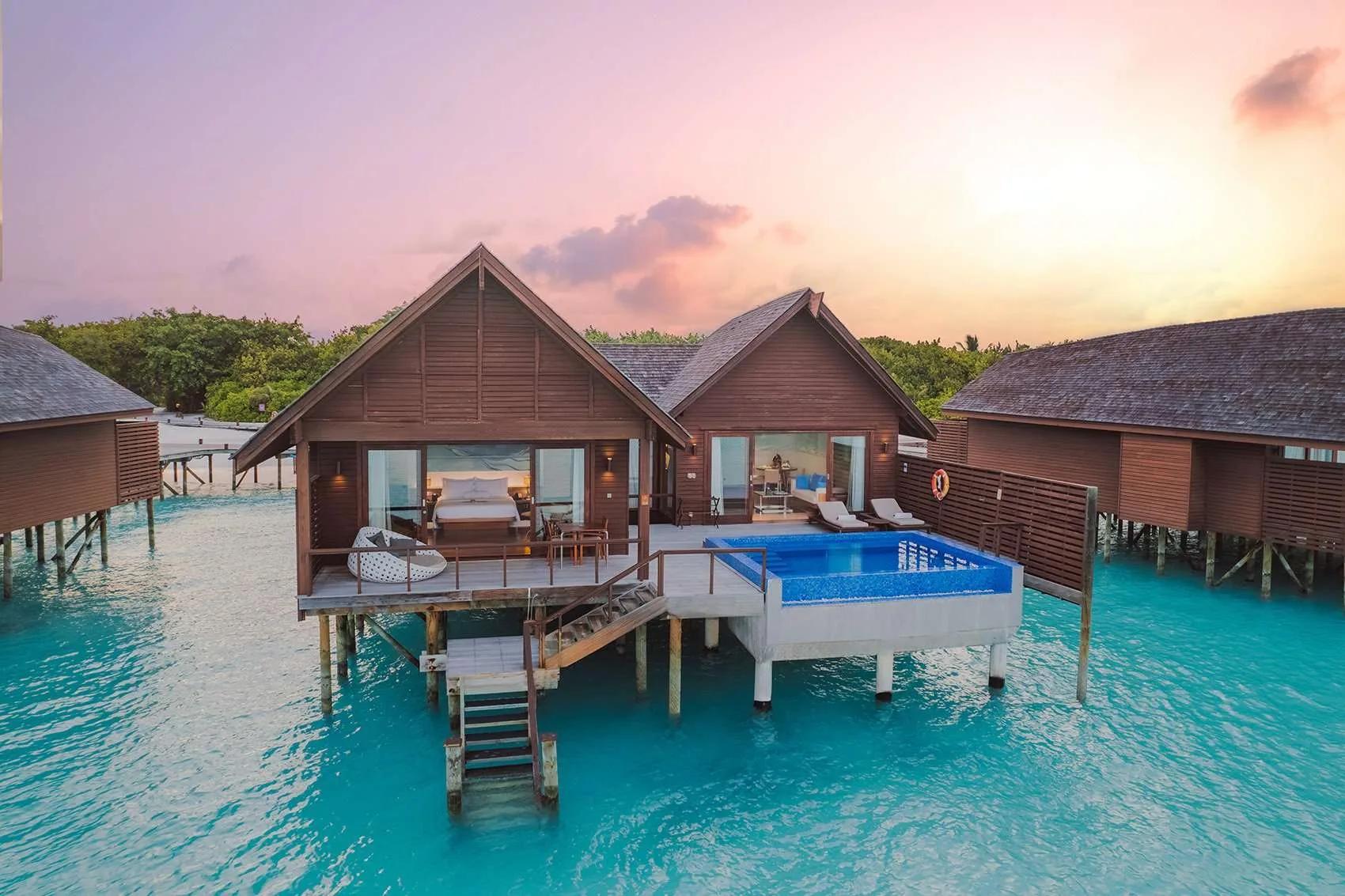 Two overwater Ocean Villas with Pool at dusk, their private pools lit blue above the lagoon