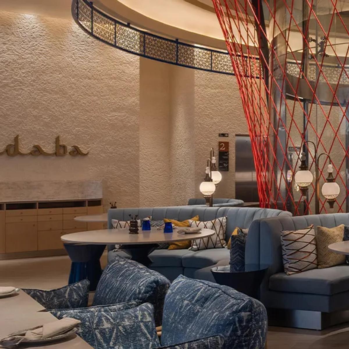 Hadaba's dining room at SO/ Maldives, curved blue banquette seating beneath a suspended red string installation, lit for the evening