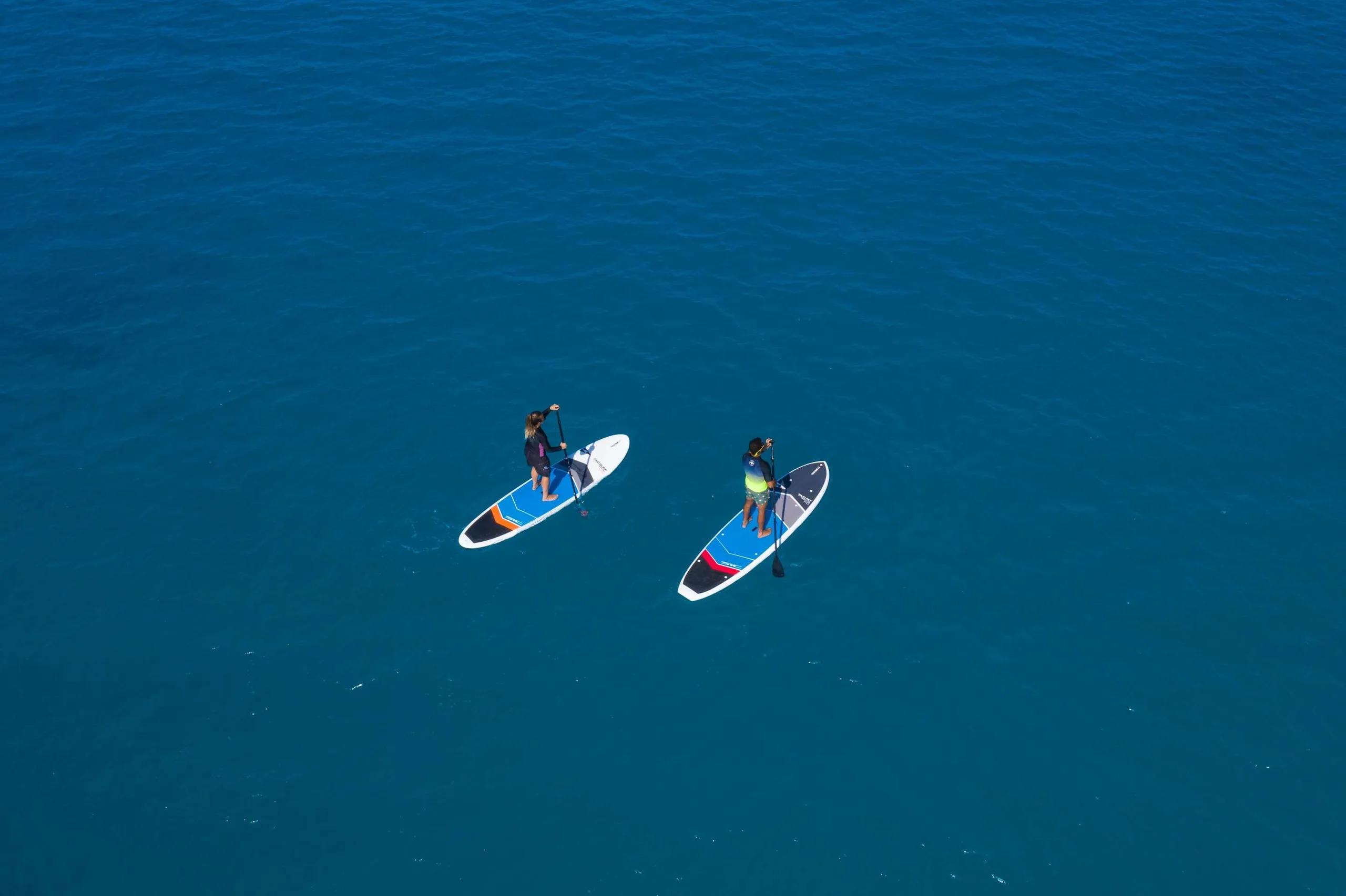 Two guests paddleboarding across open blue water near Radisson Blu Resort Maldives, seen from above