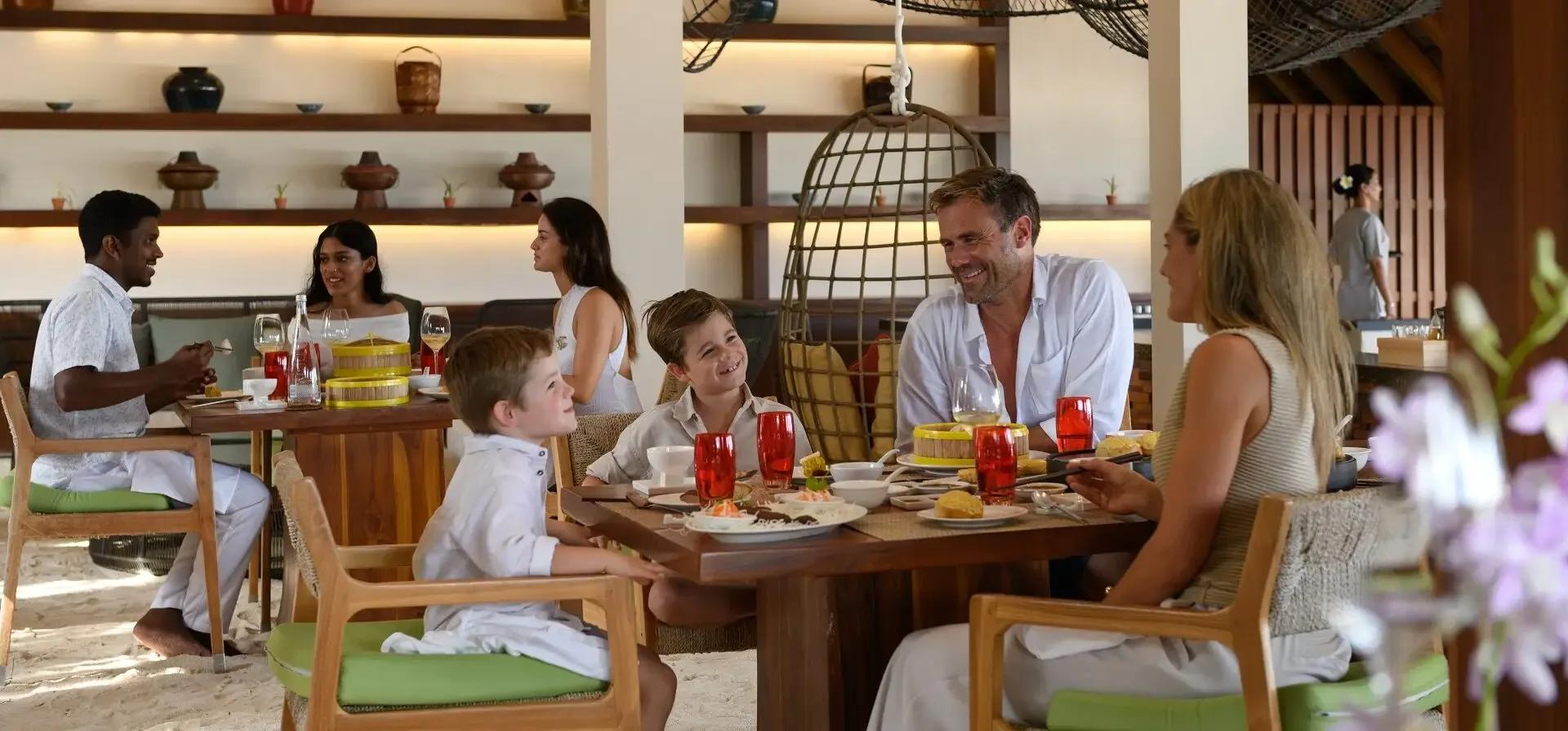 A family sharing dim sum and hot pot dishes at Ufaa's open-air, sand-floored dining room at Conrad Maldives Rangali