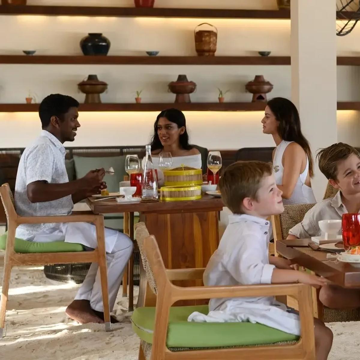A family sharing dim sum and hot pot dishes at Ufaa's open-air, sand-floored dining room at Conrad Maldives Rangali
