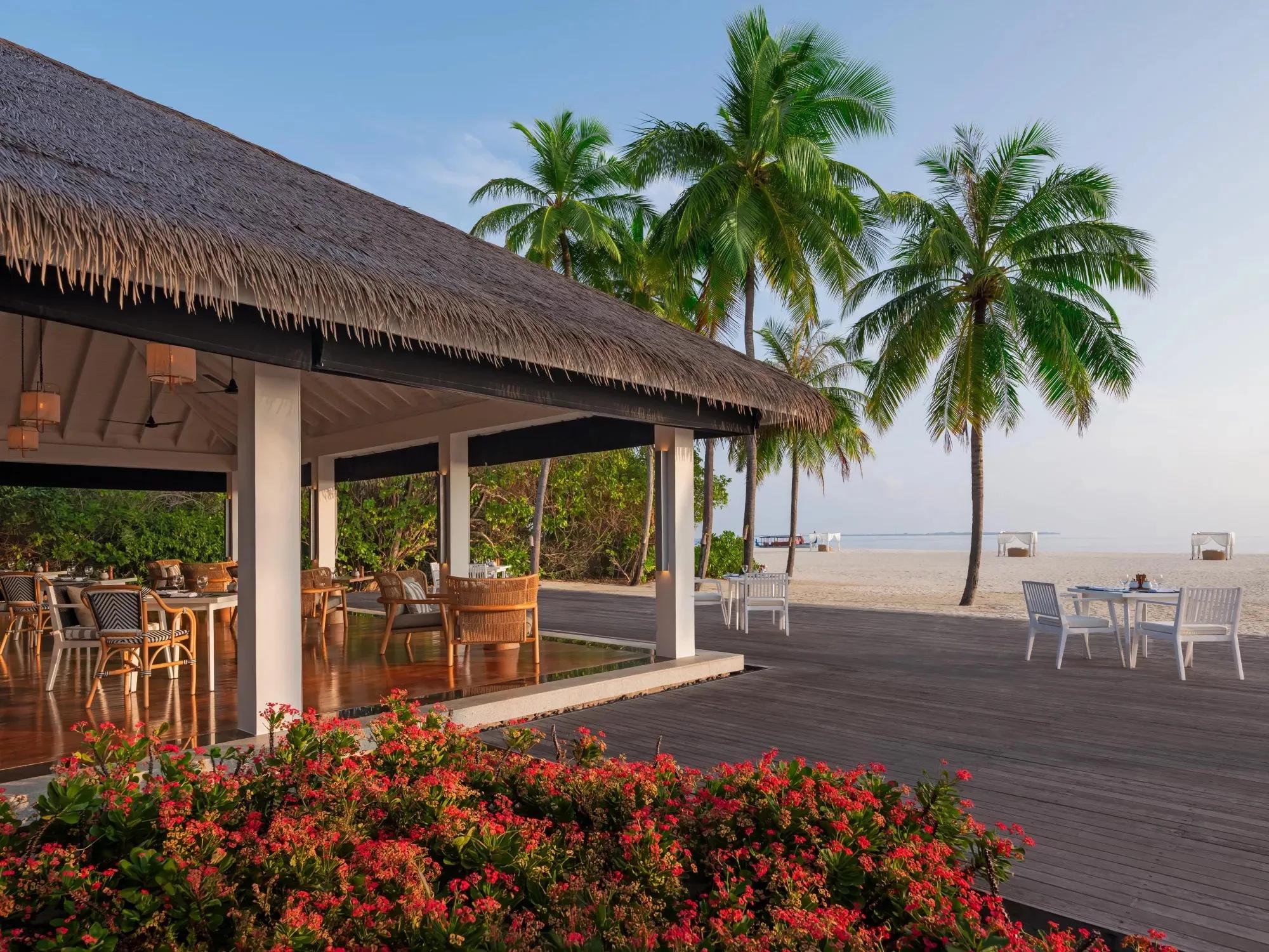 Palms Restaurant's beachfront terrace at Noku Maldives, tables set beneath palms steps from the sand