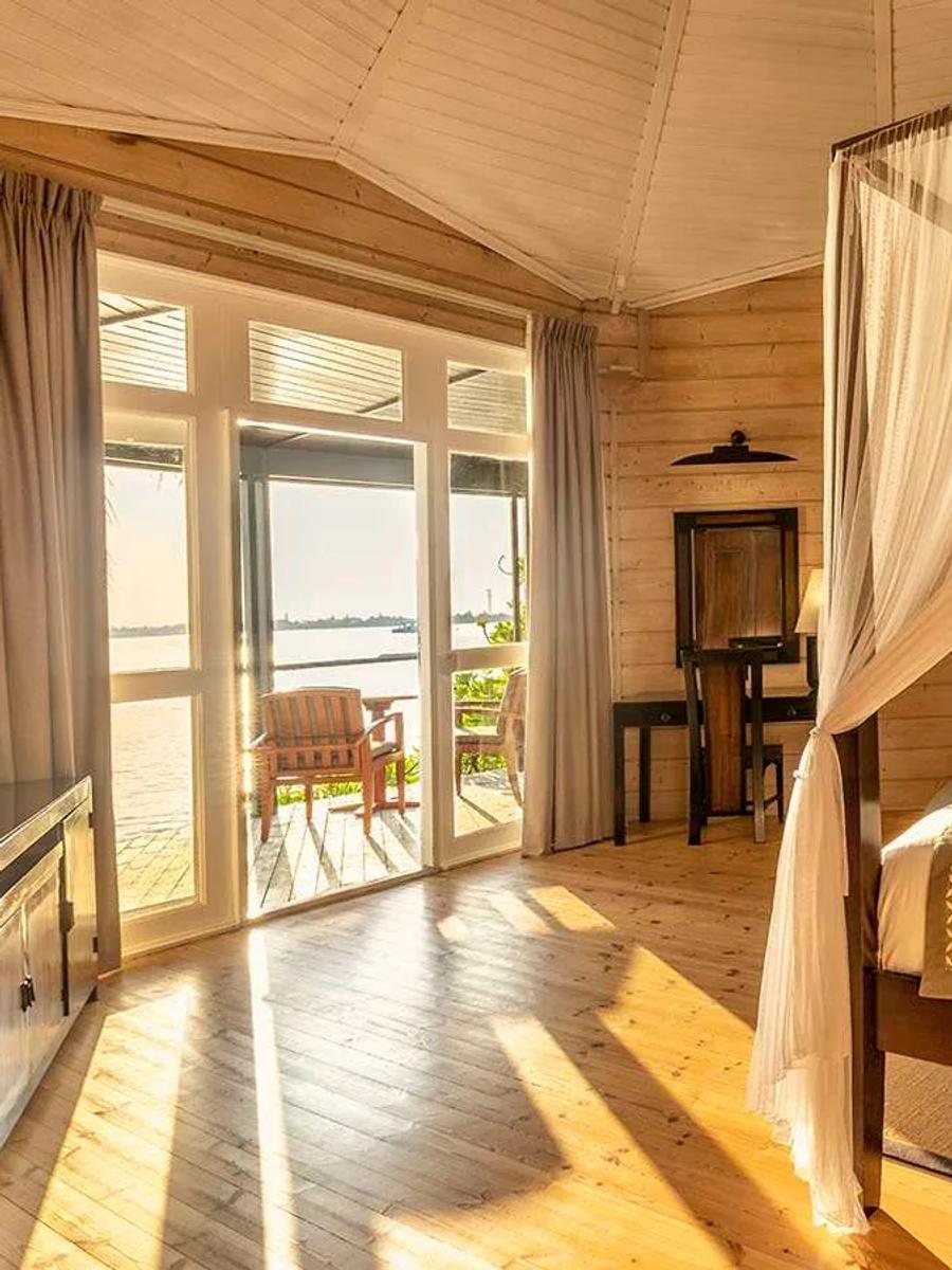 The interior of a Premium Jacuzzi Beach Villa, a four-poster bed beneath a peaked timber ceiling with the beach visible through the open doors