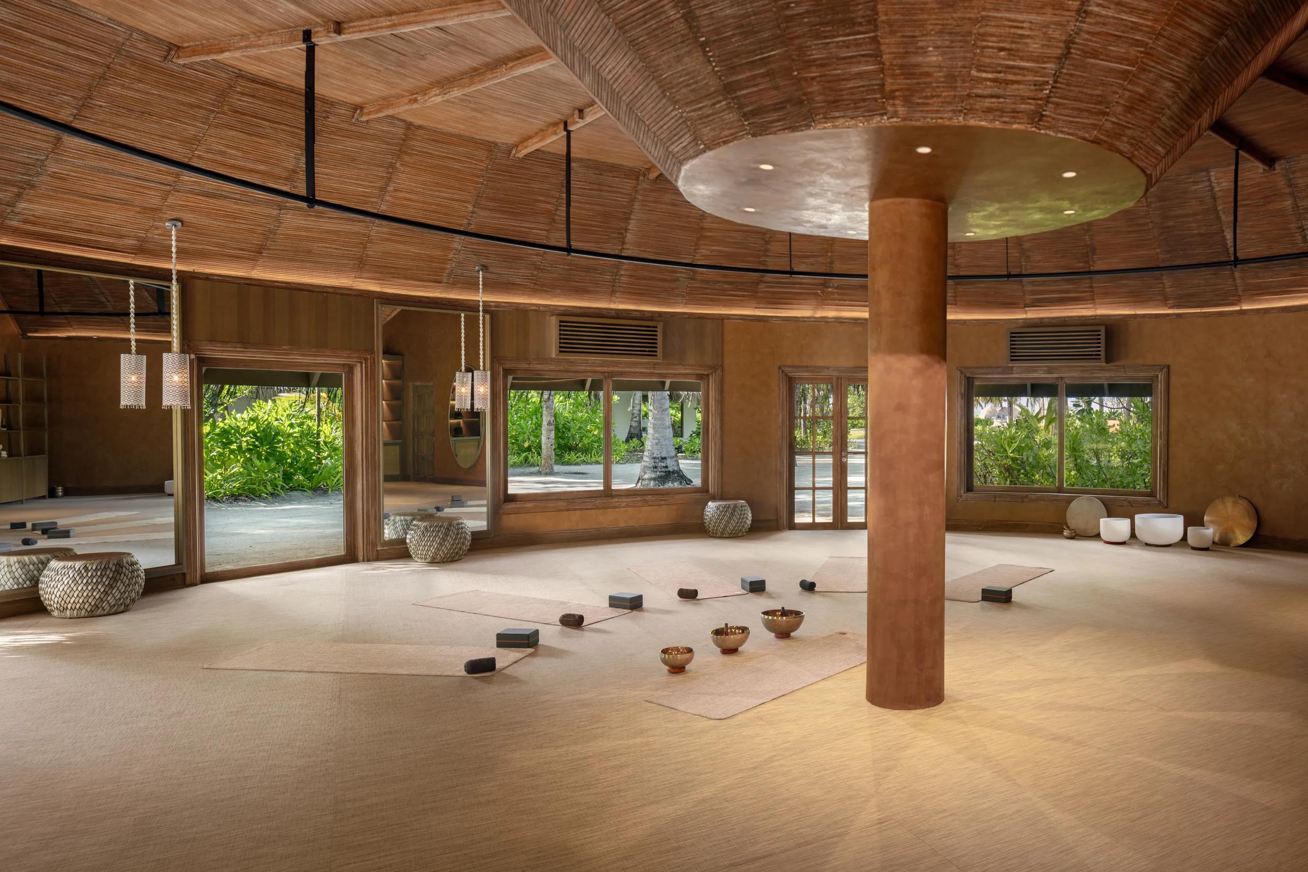 A circular yoga studio with mats and singing bowls laid out on the floor beneath a woven, domed thatched ceiling.