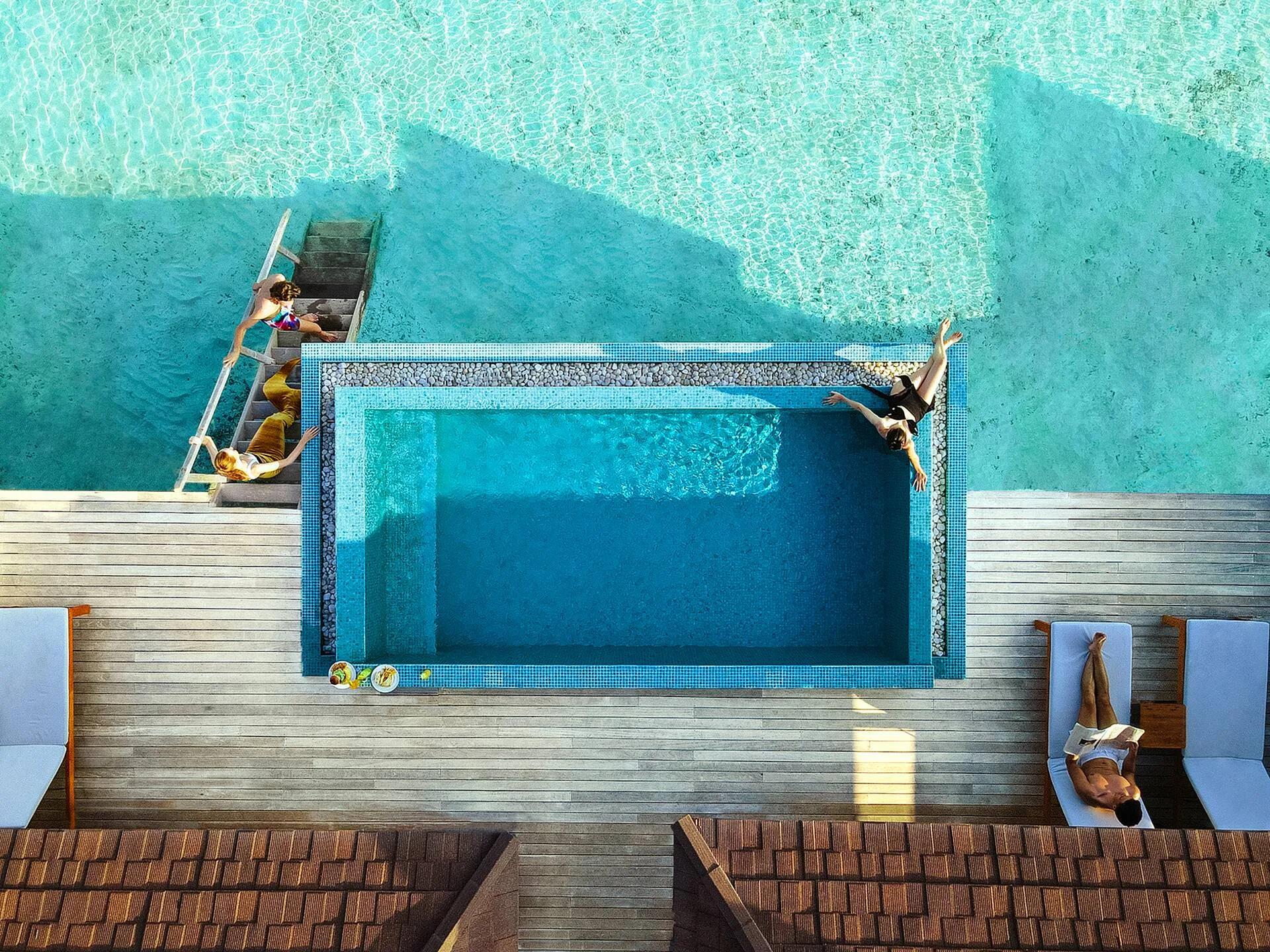 Two guests jumping into the shared plunge pool of a Two Bedroom Lagoon Overwater Villa, seen from directly above