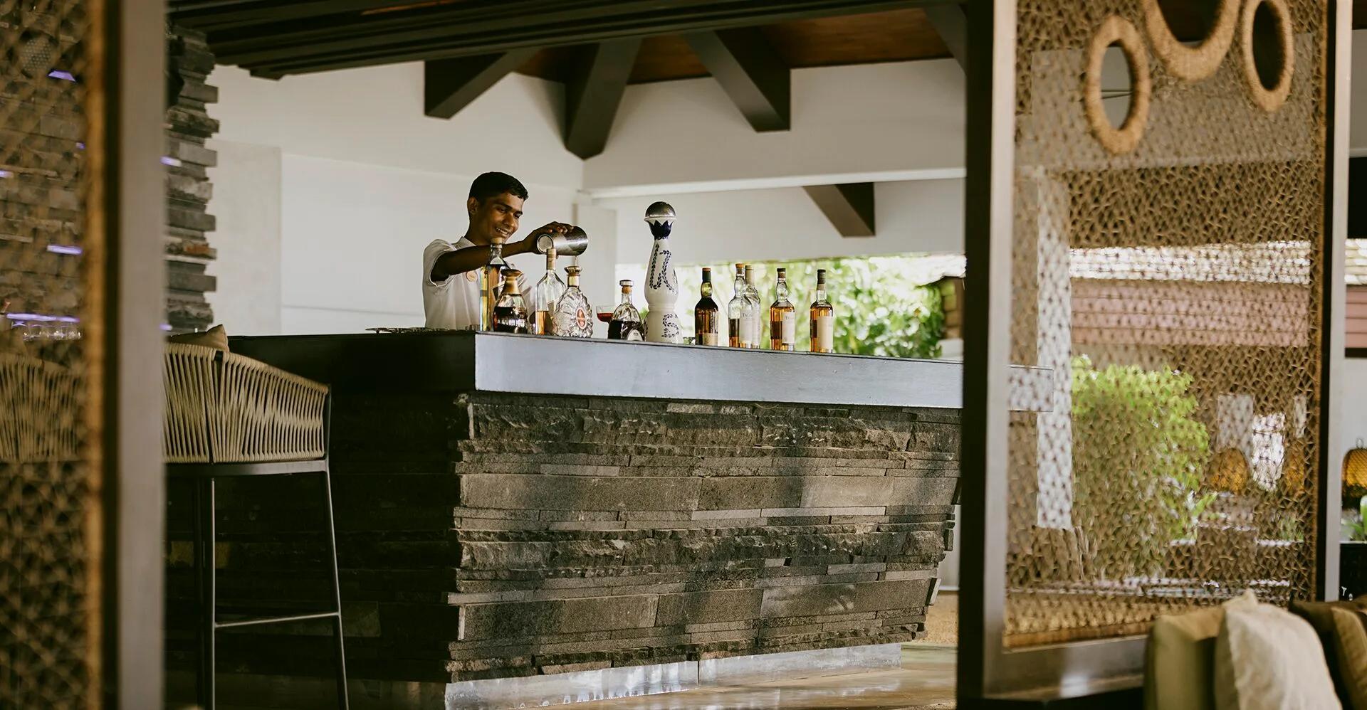A bartender pouring a drink behind the stacked-stone bar at Fen Bar, bottles lined up on the counter