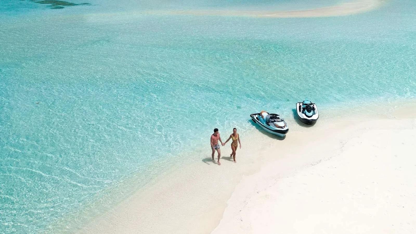A couple walking along the shallows beside two jet skis on a sandbank at Jawakara