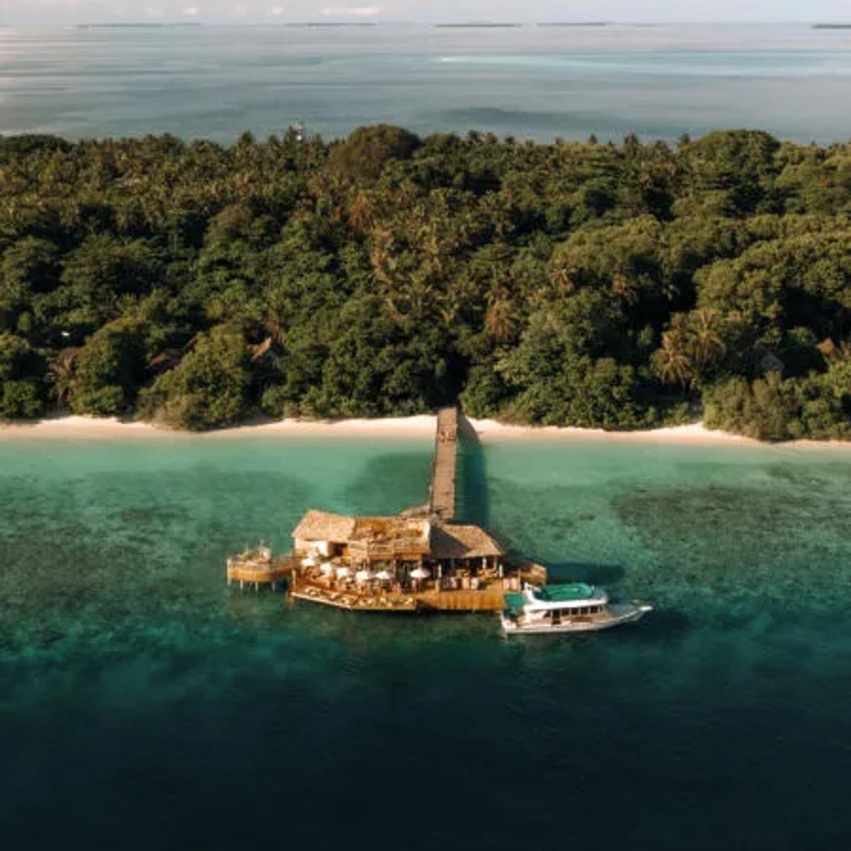 An aerial view of Out of the Sea's rustic shoreline pavilion on stilts, a boat moored alongside and jungle behind