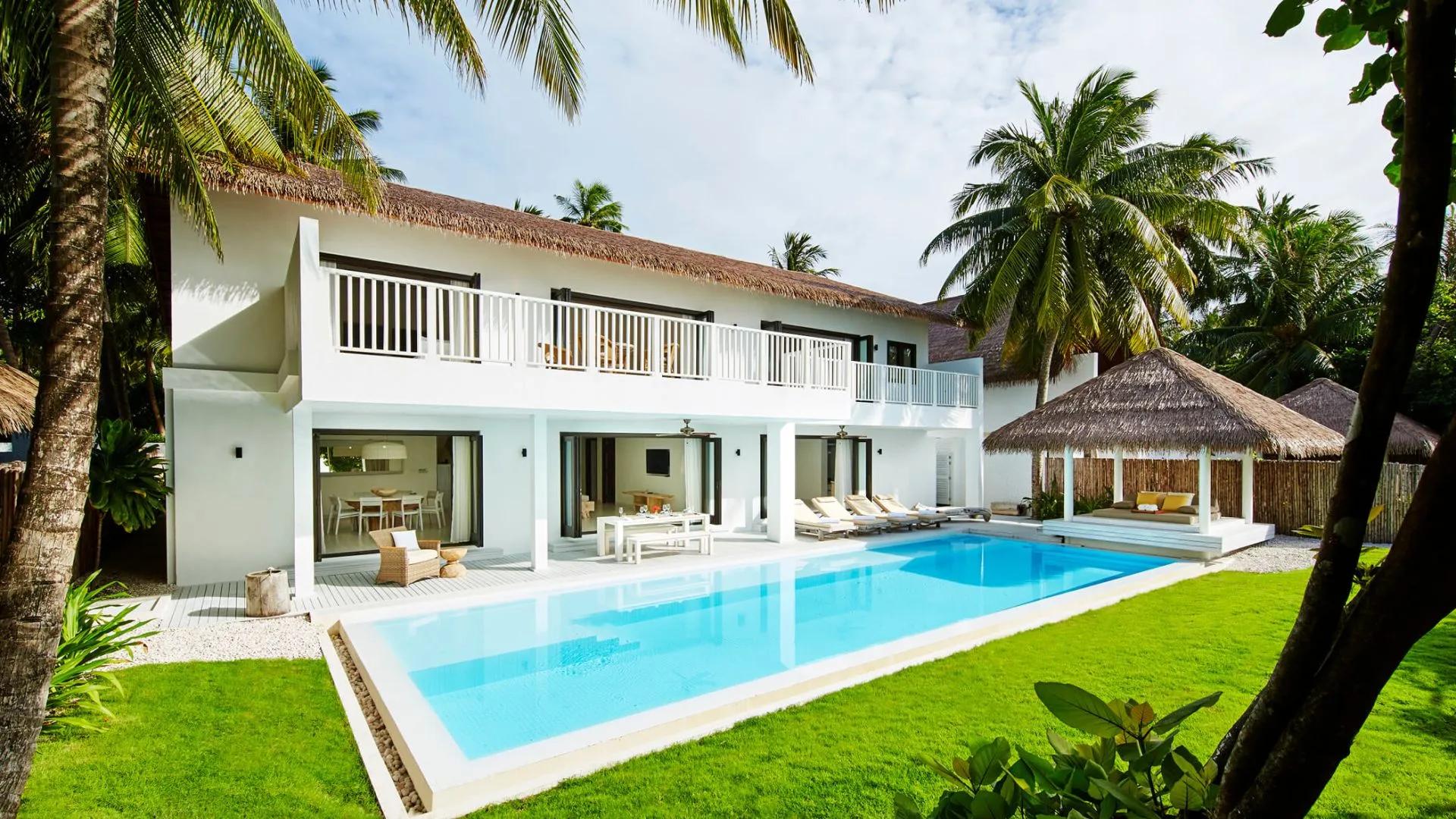 Two-storey COMO Residence with its private pool and lawn, palm trees framing the white two-storey house