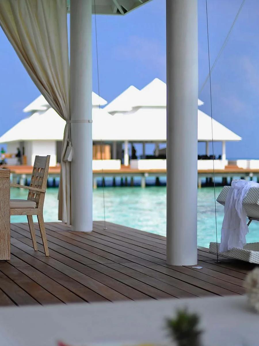 A guest lounging on the deck of a One Bedroom Water Villa at Diamonds Athuruga, water villas visible beyond