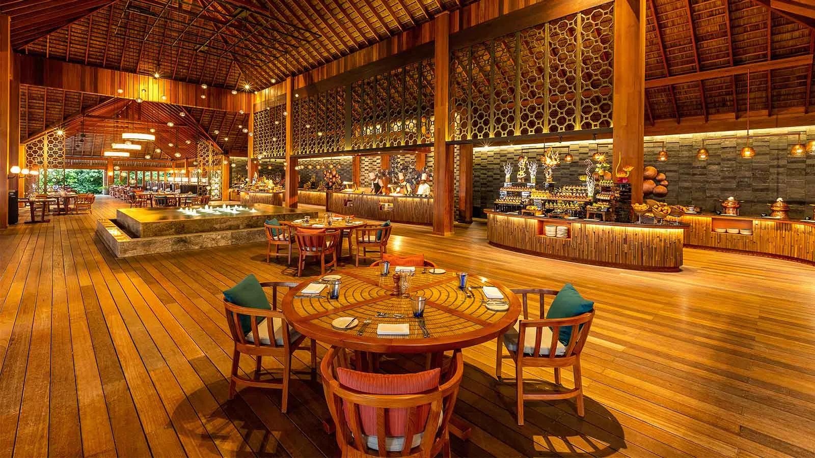 Canneli Restaurant's open-air dining room, wooden tables set beneath a high thatched roof beside the live cooking stations