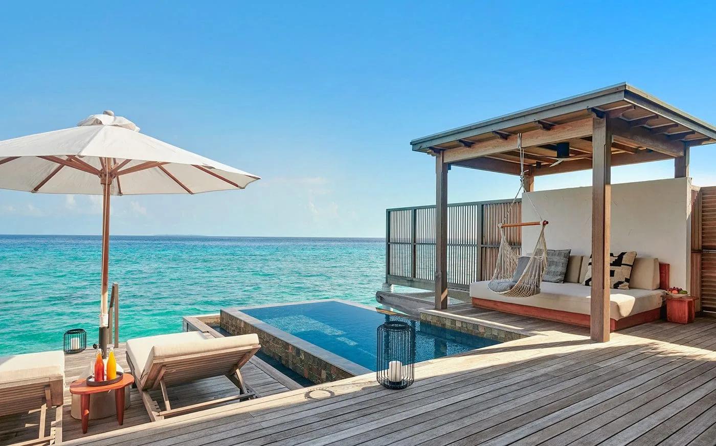 Overwater deck of a water villa with a private plunge pool, sun loungers and umbrella, open ocean beyond