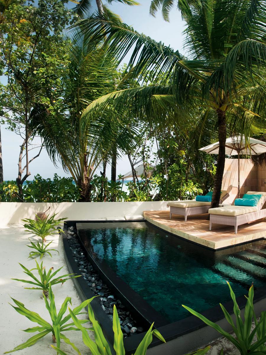 A Family Beach Villa's private plunge pool and sun loungers under a thatched umbrella, set in a garden with a low wall and the ocean visible beyond