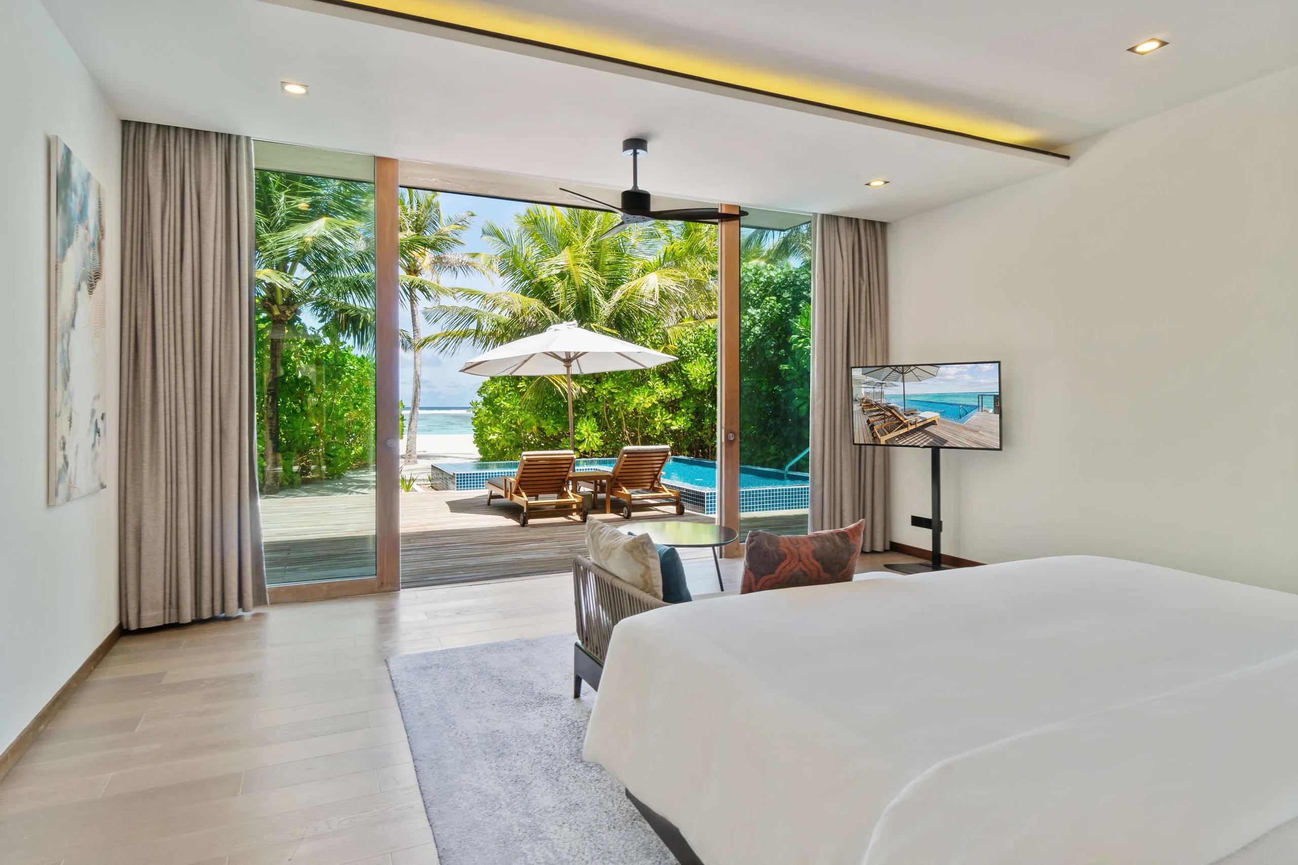 The bedroom of a Two Bedroom Beach Villa at Radisson Blu Resort Maldives, sliding doors open to its private pool deck