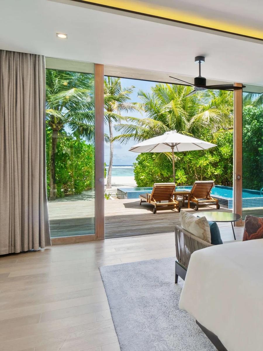 The bedroom of a Two Bedroom Beach Villa at Radisson Blu Resort Maldives, sliding doors open to its private pool deck