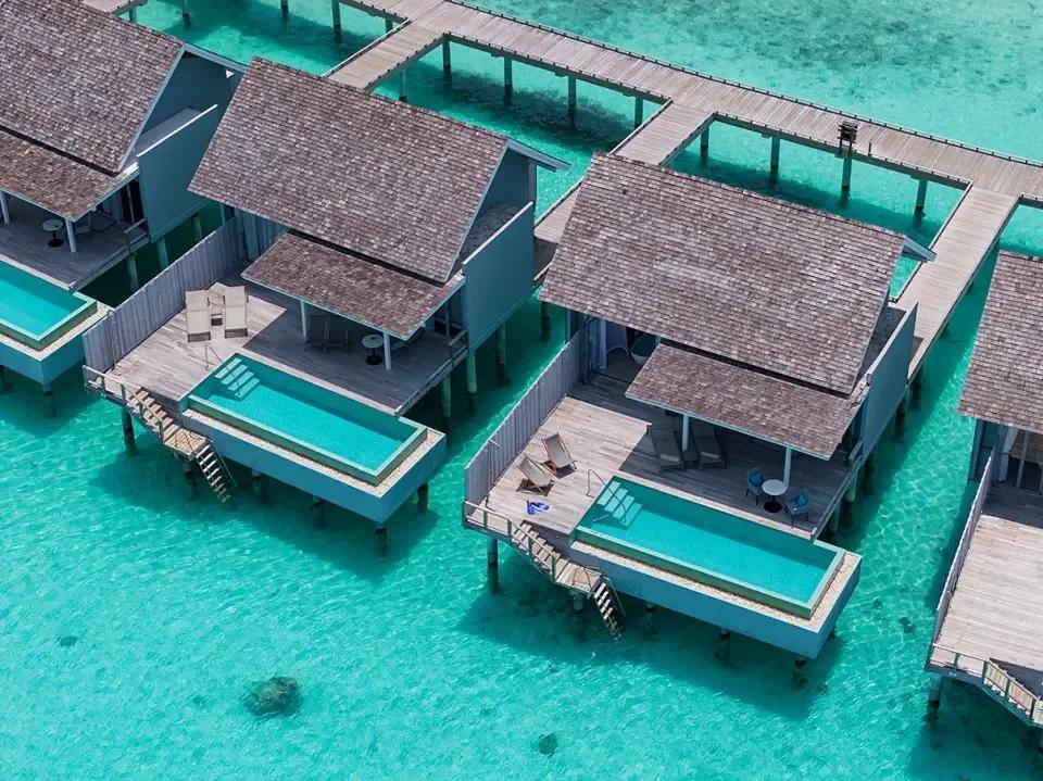 Aerial view of Water Villa with Pool units over the lagoon, each with a private plunge pool and a curving wooden jetty connecting them