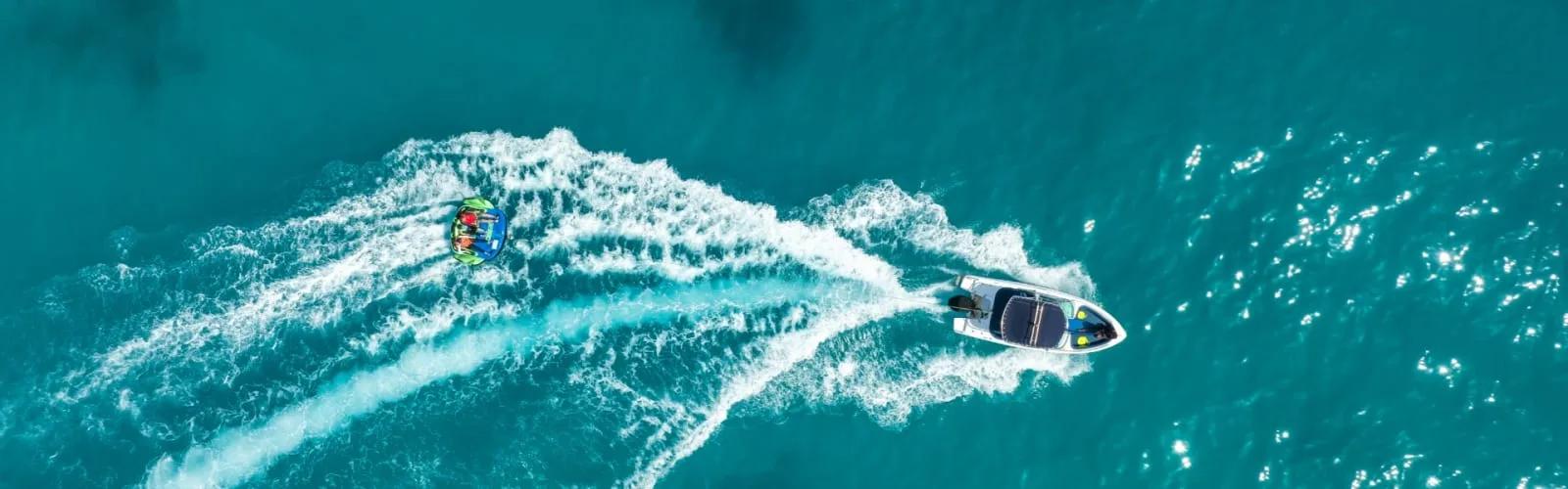A guest riding an inflatable fun tube behind a speedboat at Avani+ Fares Maldives Resort