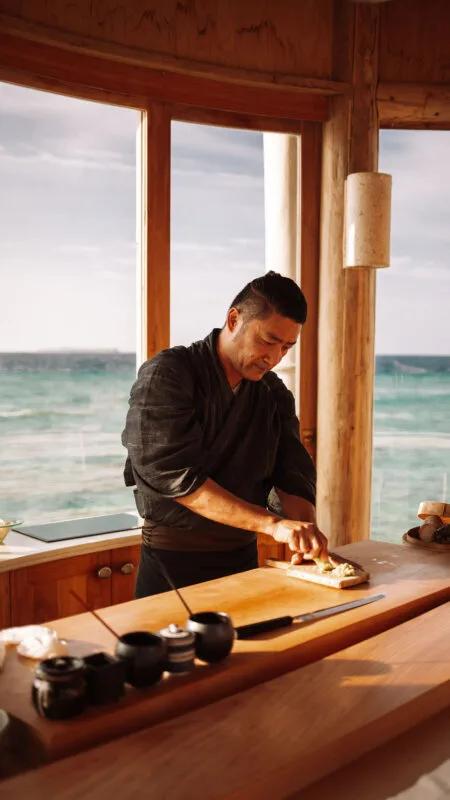 Chef Akira prepares a dish at the six-seat sushi counter, floor-to-ceiling windows opening onto open water behind him