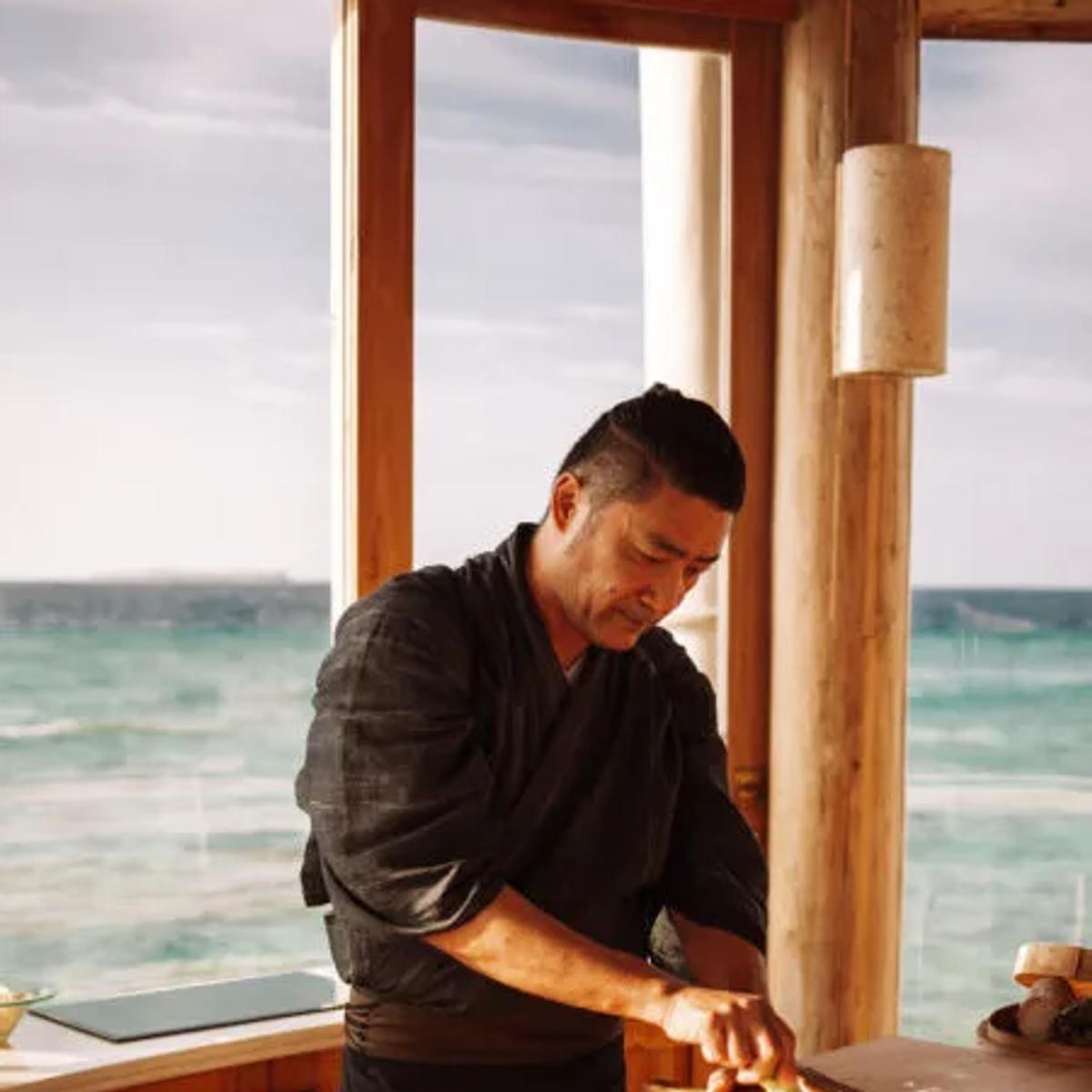 Chef Akira prepares a dish at the six-seat sushi counter, floor-to-ceiling windows opening onto open water behind him