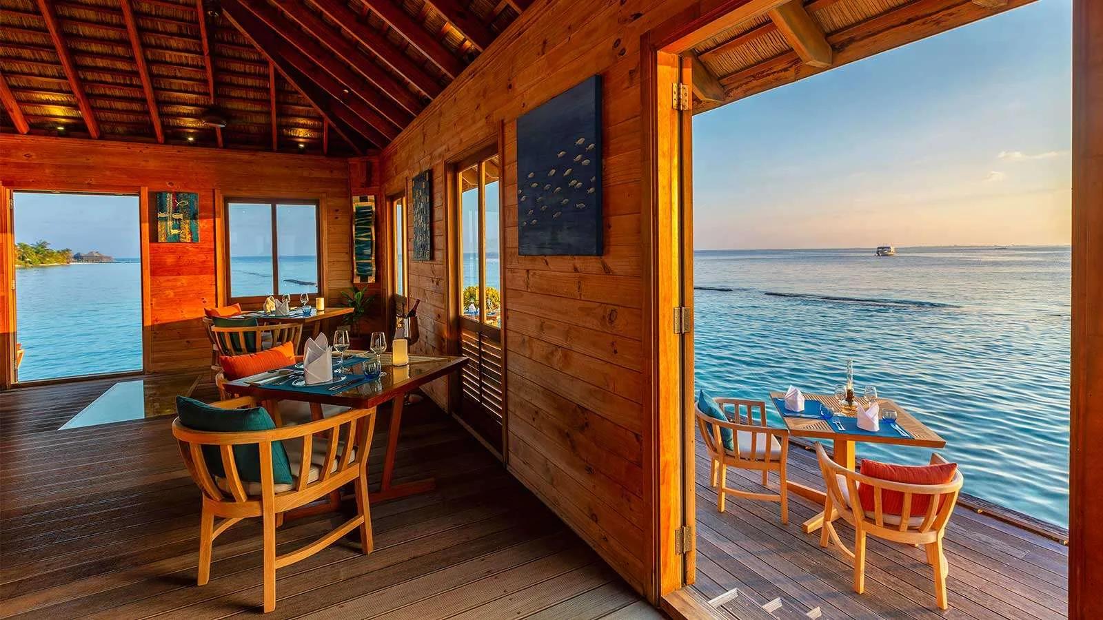Aqua Restaurant's dining room at sunset, tables set both indoors and on the open deck facing the ocean