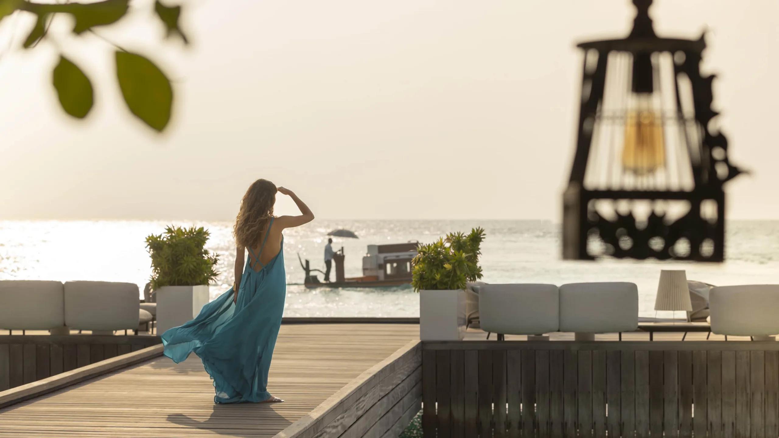 A guest in a blue dress watching a dhoni arrive at the jetty at golden hour