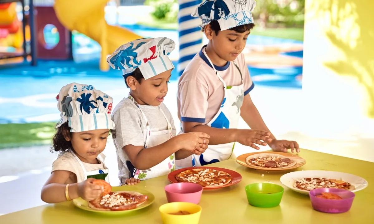 Three children in chef hats decorating their own pizzas at a Kandiland activity table