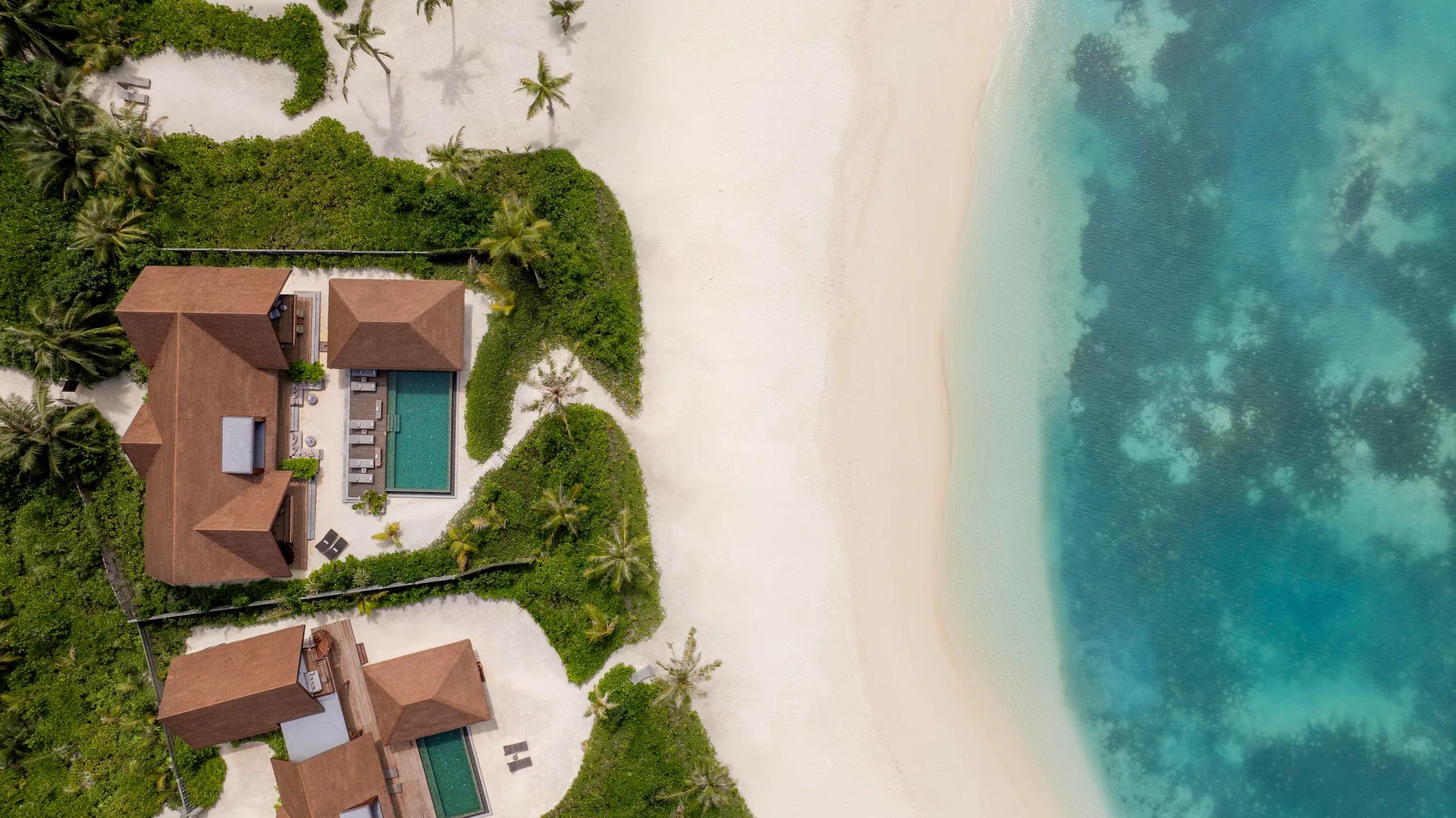 Aerial view of two large beachfront villas, each with a private pool, framed by garden and beach.