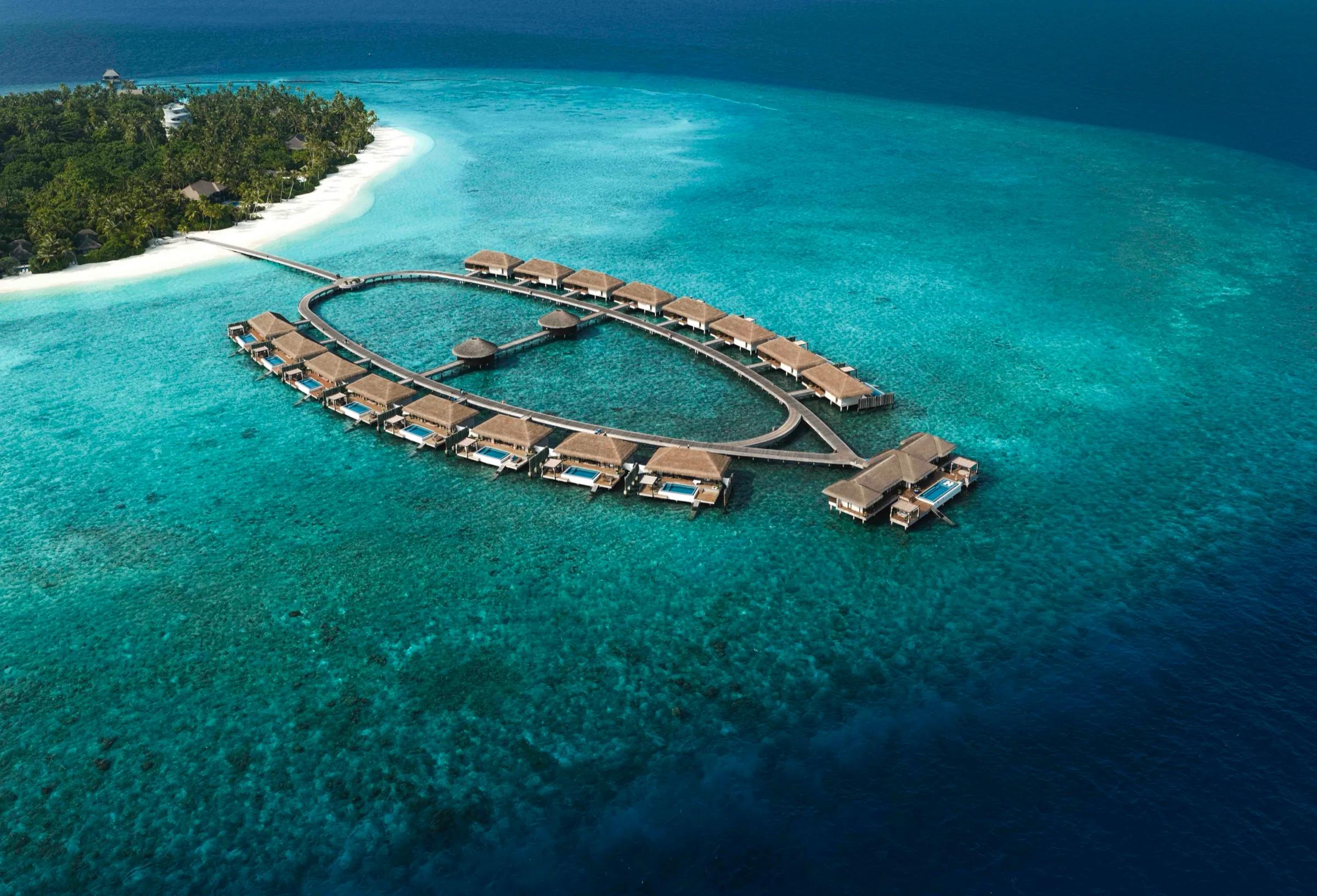 An aerial view of Velaa's overwater villa loop, thatched roofs ringed by a wooden walkway over pale turquoise water