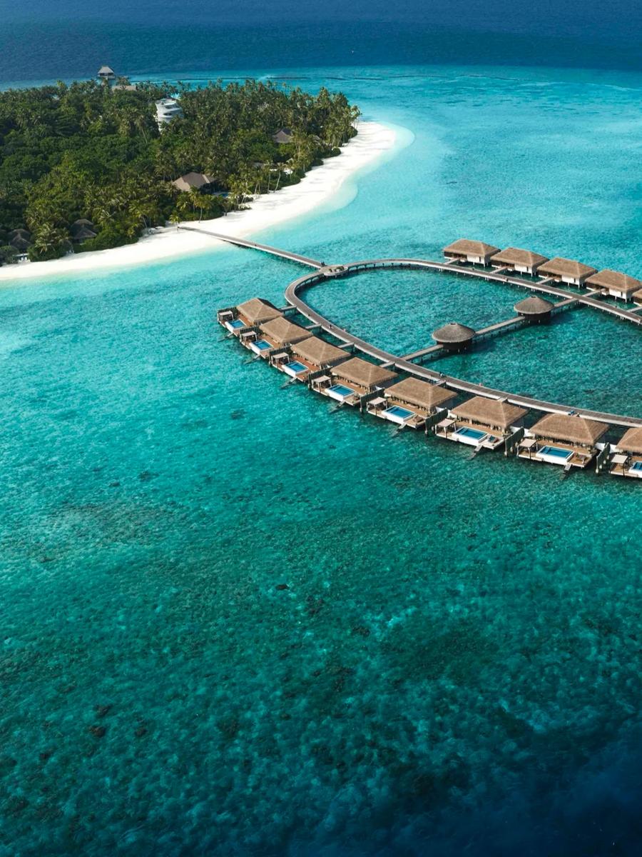 An aerial view of Velaa's overwater villa loop, thatched roofs ringed by a wooden walkway over pale turquoise water