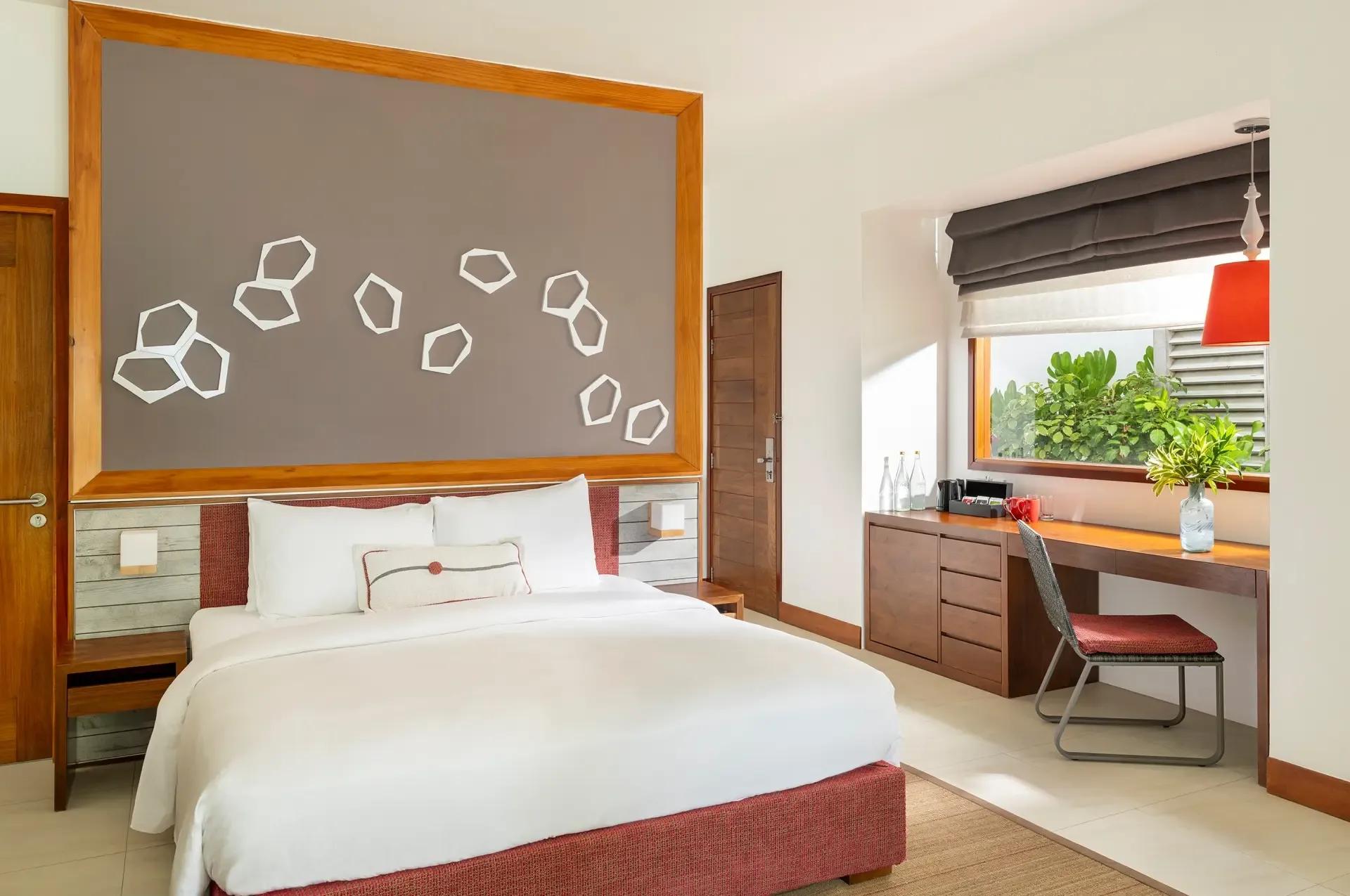 Interior of a Deluxe Beach Bungalow at Niva Dhigali, king bed set against a wood-framed headboard panel
