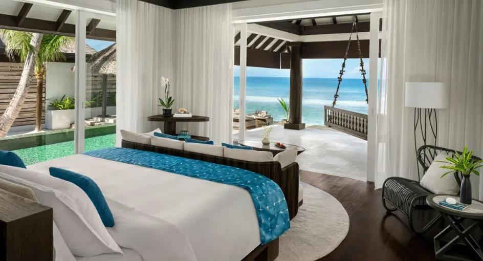 A Two-Bedroom Ocean House with Pool's bedroom opening onto the pool deck, a hanging swing daybed on the ocean-view terrace beyond