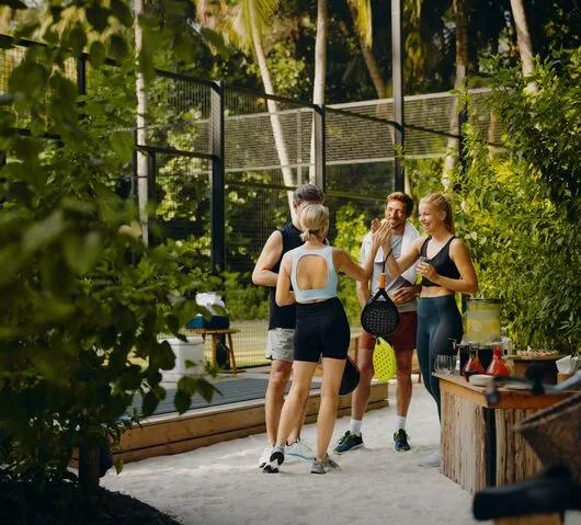 Four guests in sportswear high-fiving beside JOALI's padel court, racquets in hand