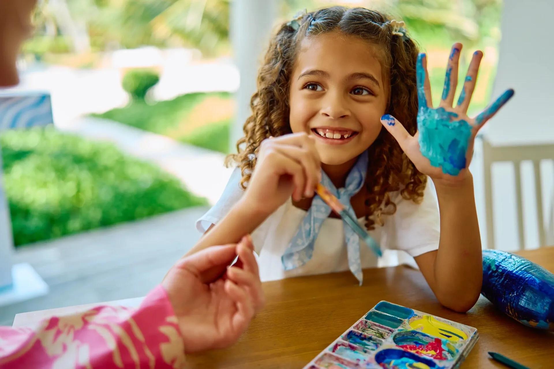 A child holding up a paint-covered hand during a pottery painting session at Jumeirah Olhahali's art studio
