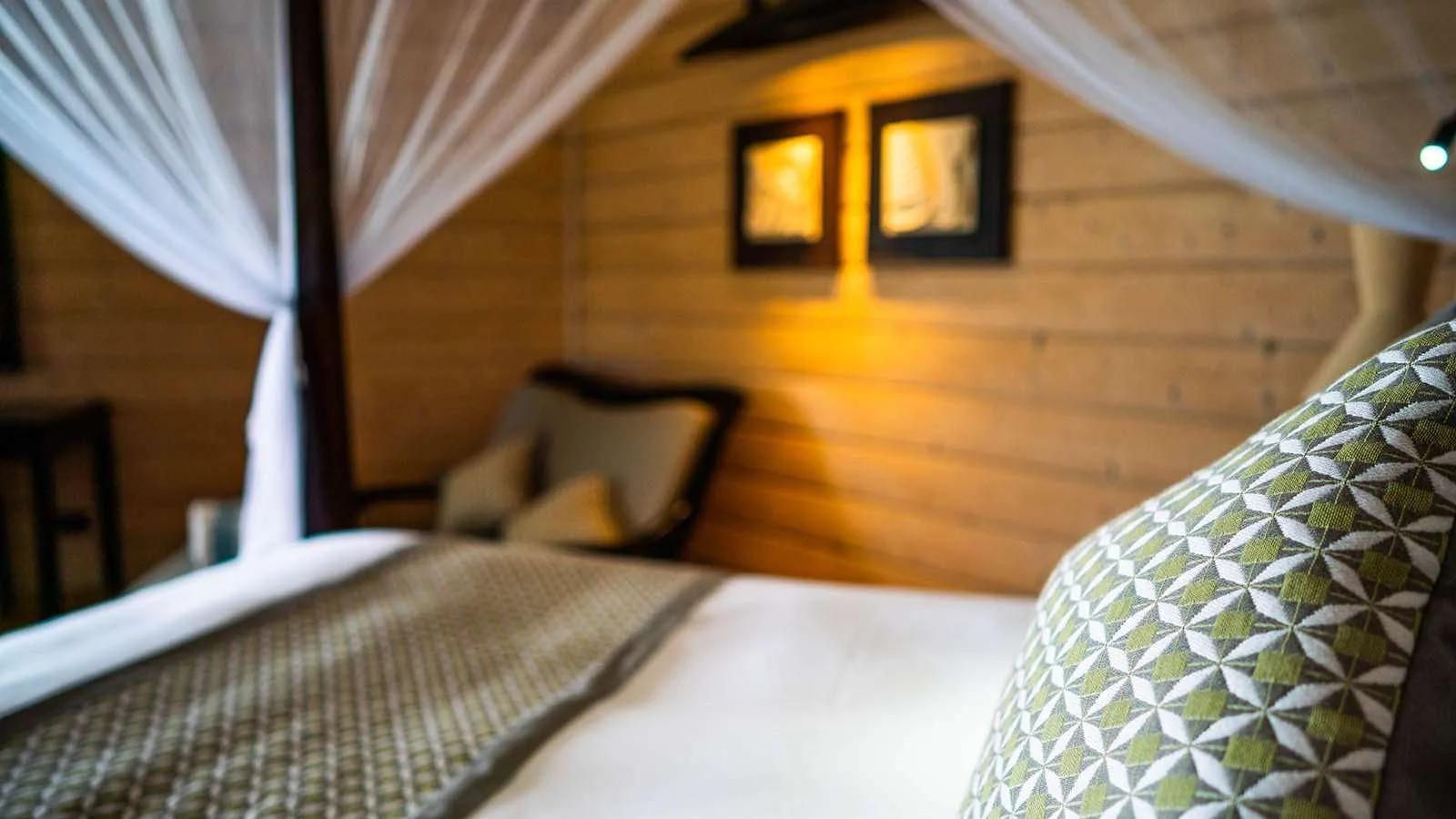 The interior of a Beach Villa, a four-poster bed with a sheer mosquito net against timber walls