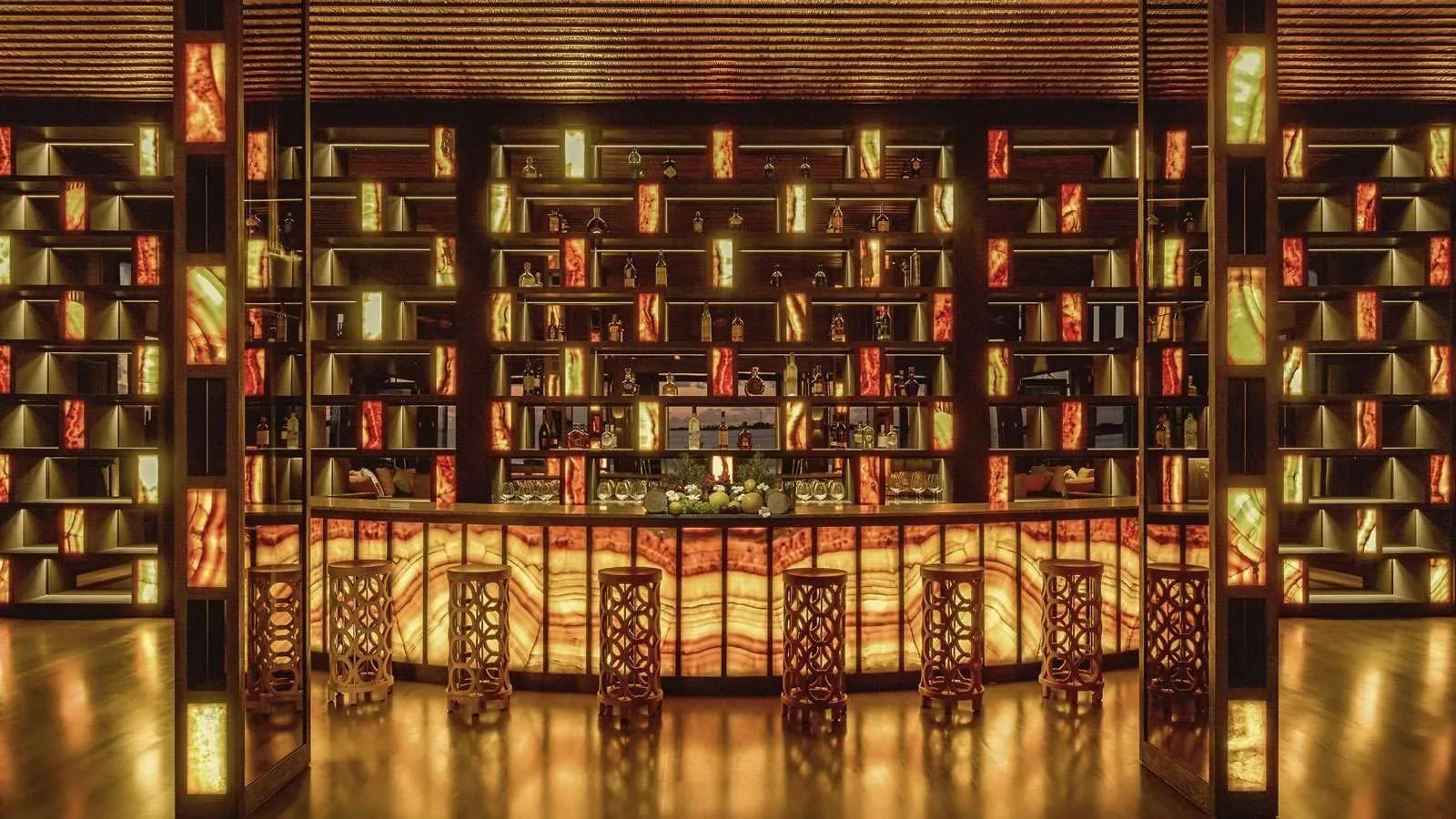 The Bar's backlit onyx shelving and curved counter, ringed with wooden stools