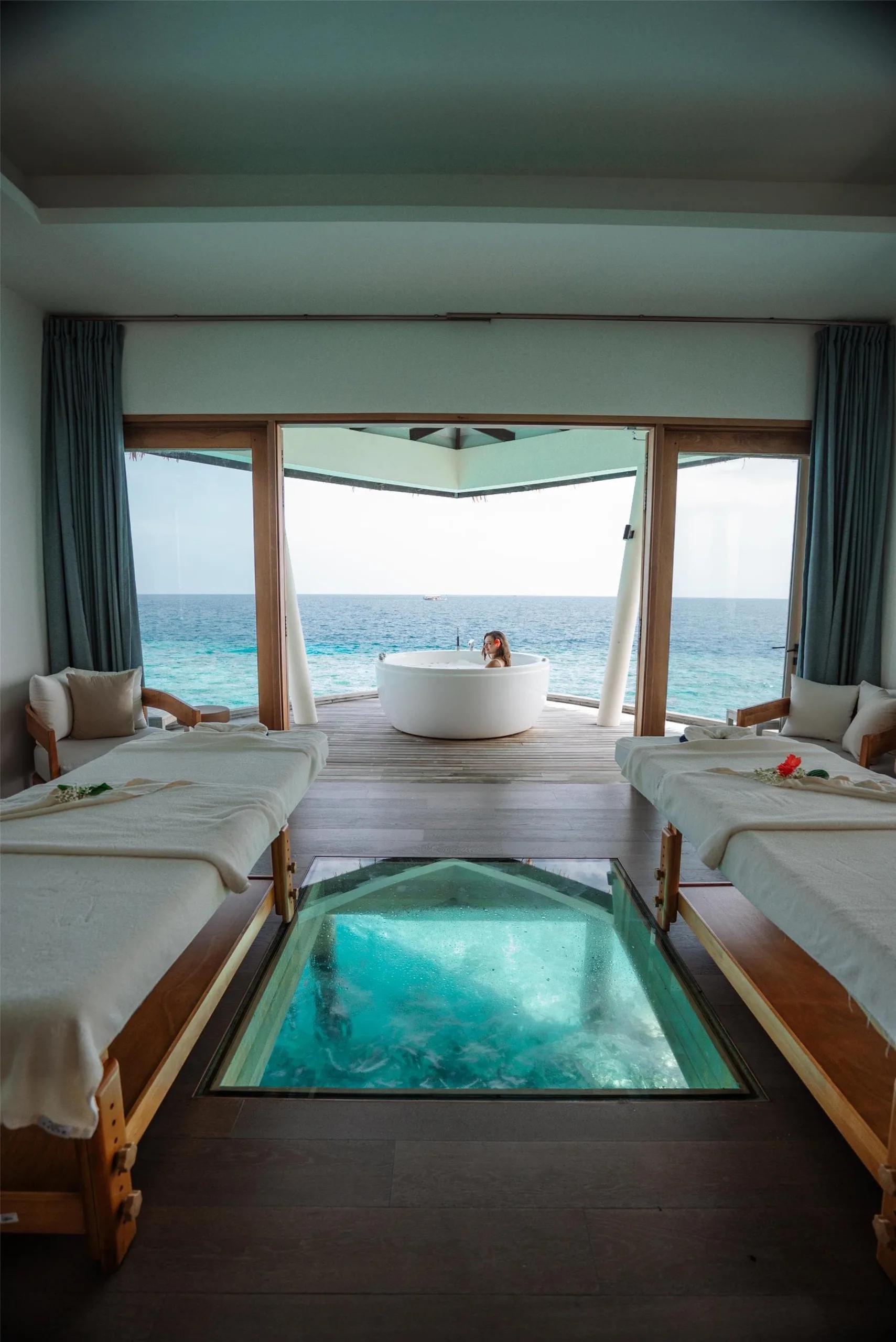One of Blu Spa's couples' treatment rooms at Radisson Blu Resort Maldives, a glass floor panel open to the water below and an outdoor tub facing the ocean