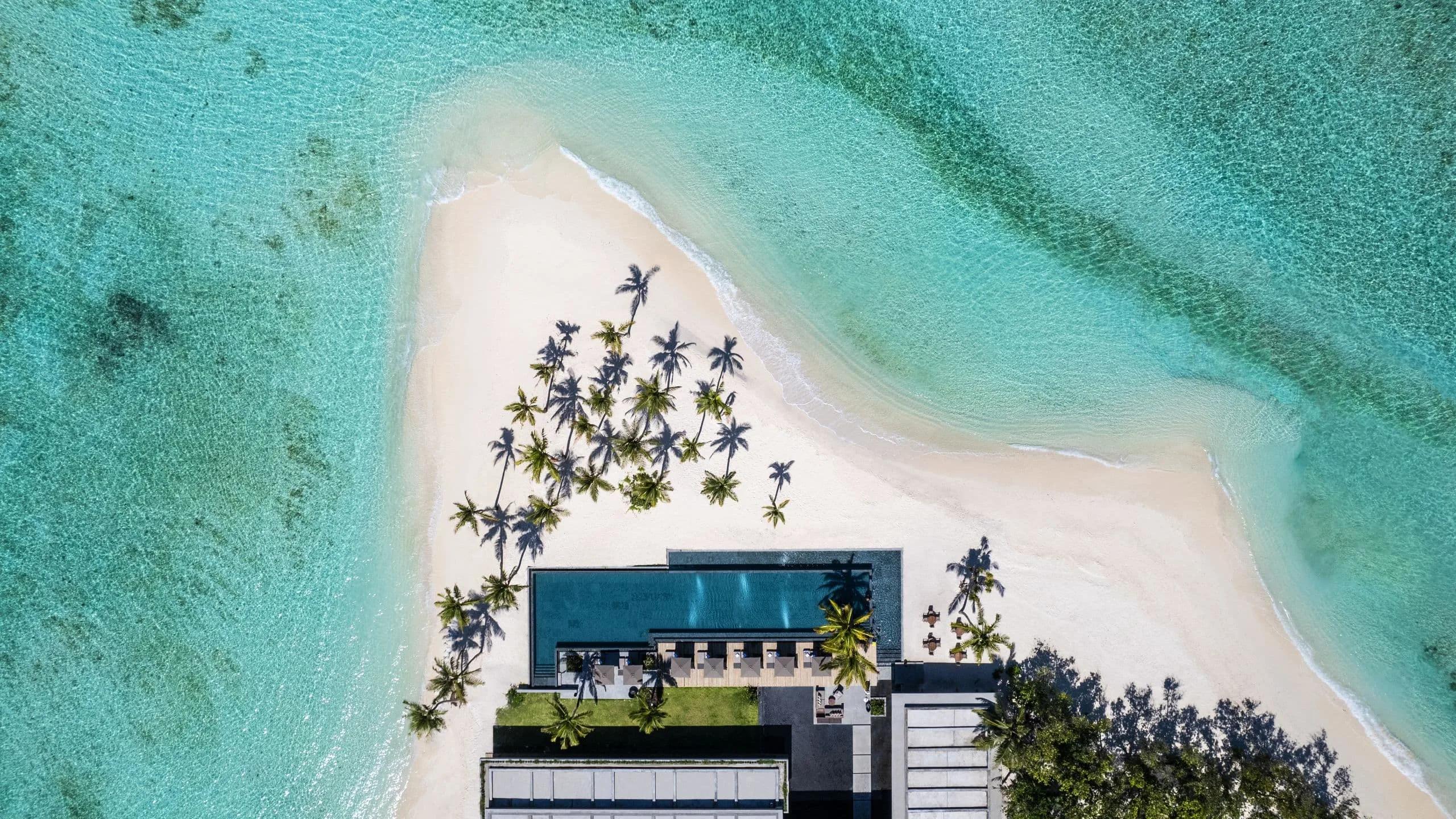 The resort's shared infinity pool seen from directly above, its far edge meeting the lagoon
