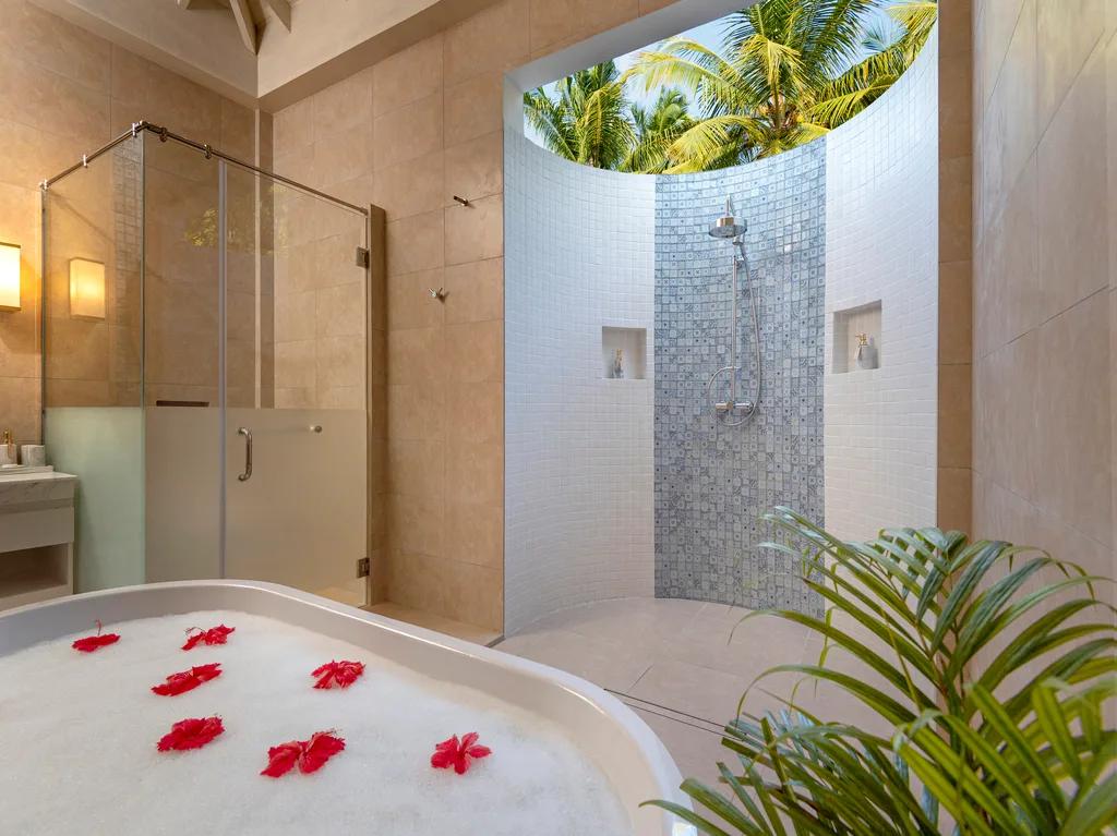 An open-air garden bathroom in a Superior Villa, with a freestanding tub scattered with red petals and a glass shower beyond