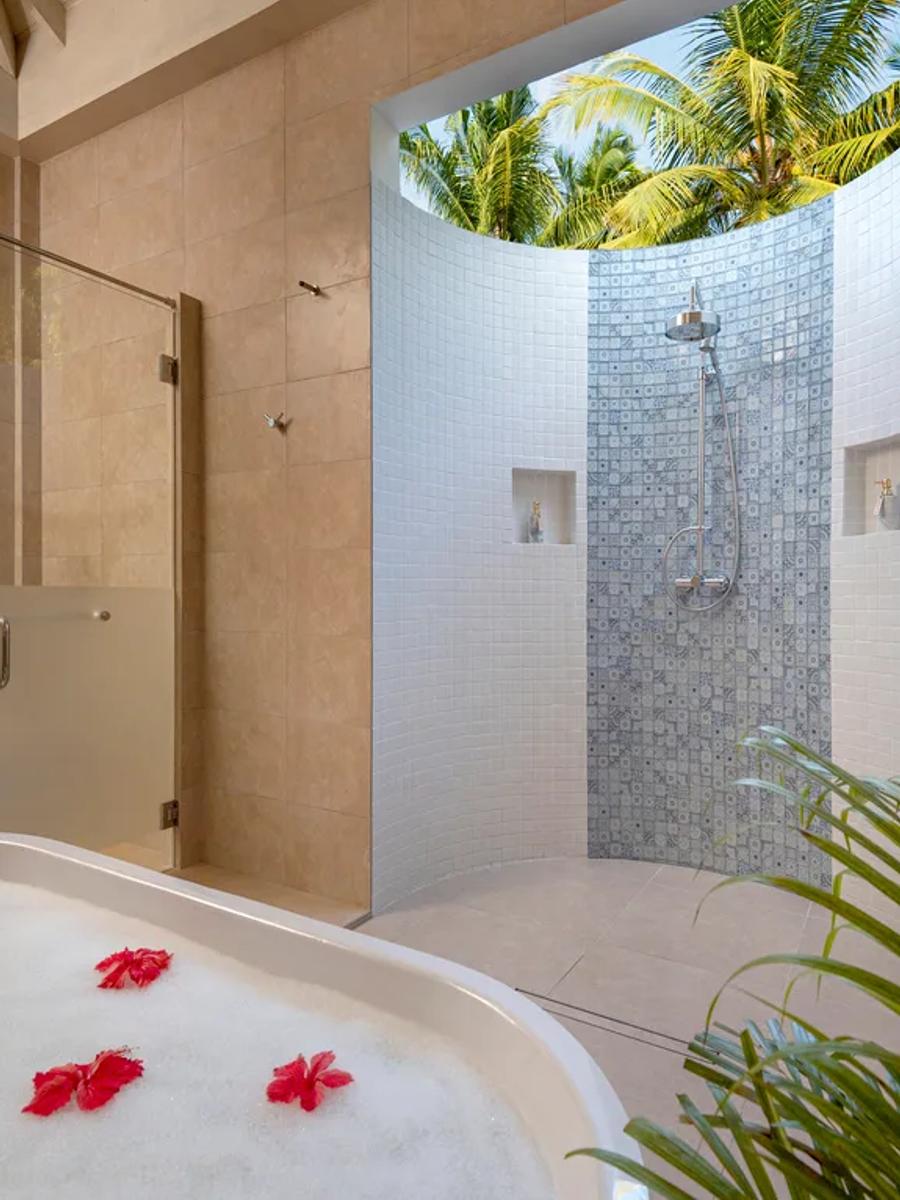 An open-air garden bathroom in a Superior Villa, with a freestanding tub scattered with red petals and a glass shower beyond